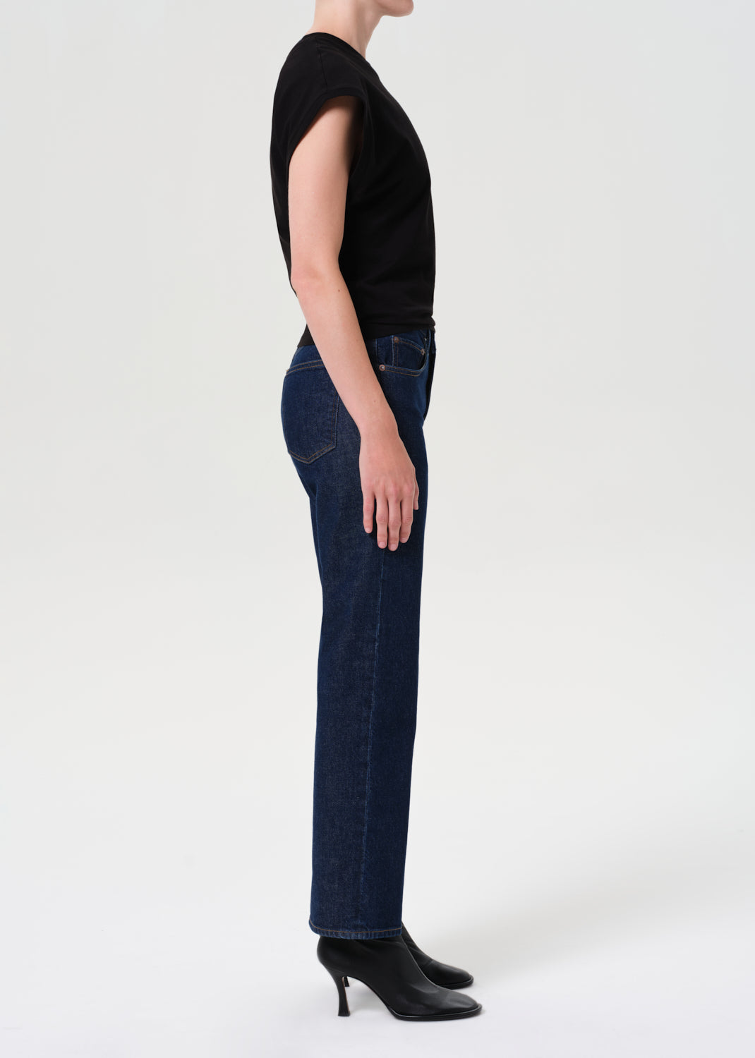 Person wearing dark blue jeans and black shoes on a white background