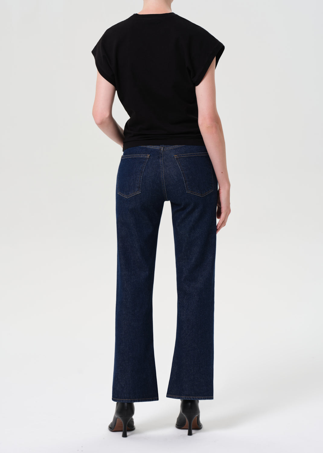 Person wearing a black top and dark blue jeans on a white background