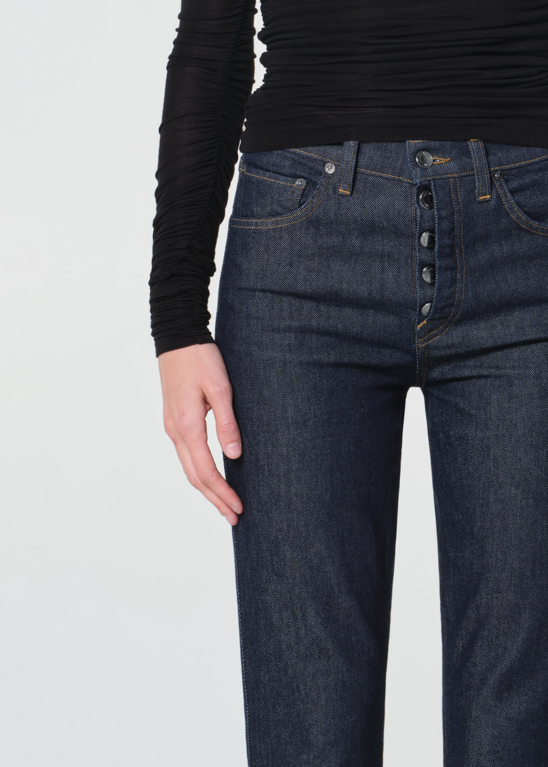 Person wearing dark blue jeans and a black long-sleeve shirt on a light gray background