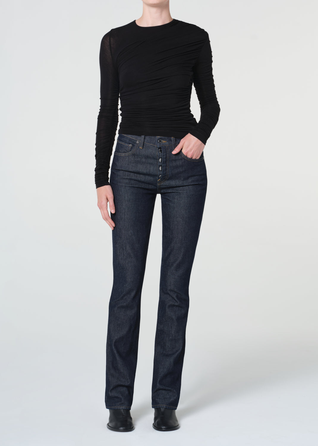 Person wearing a black long-sleeve top and dark jeans on a white background
