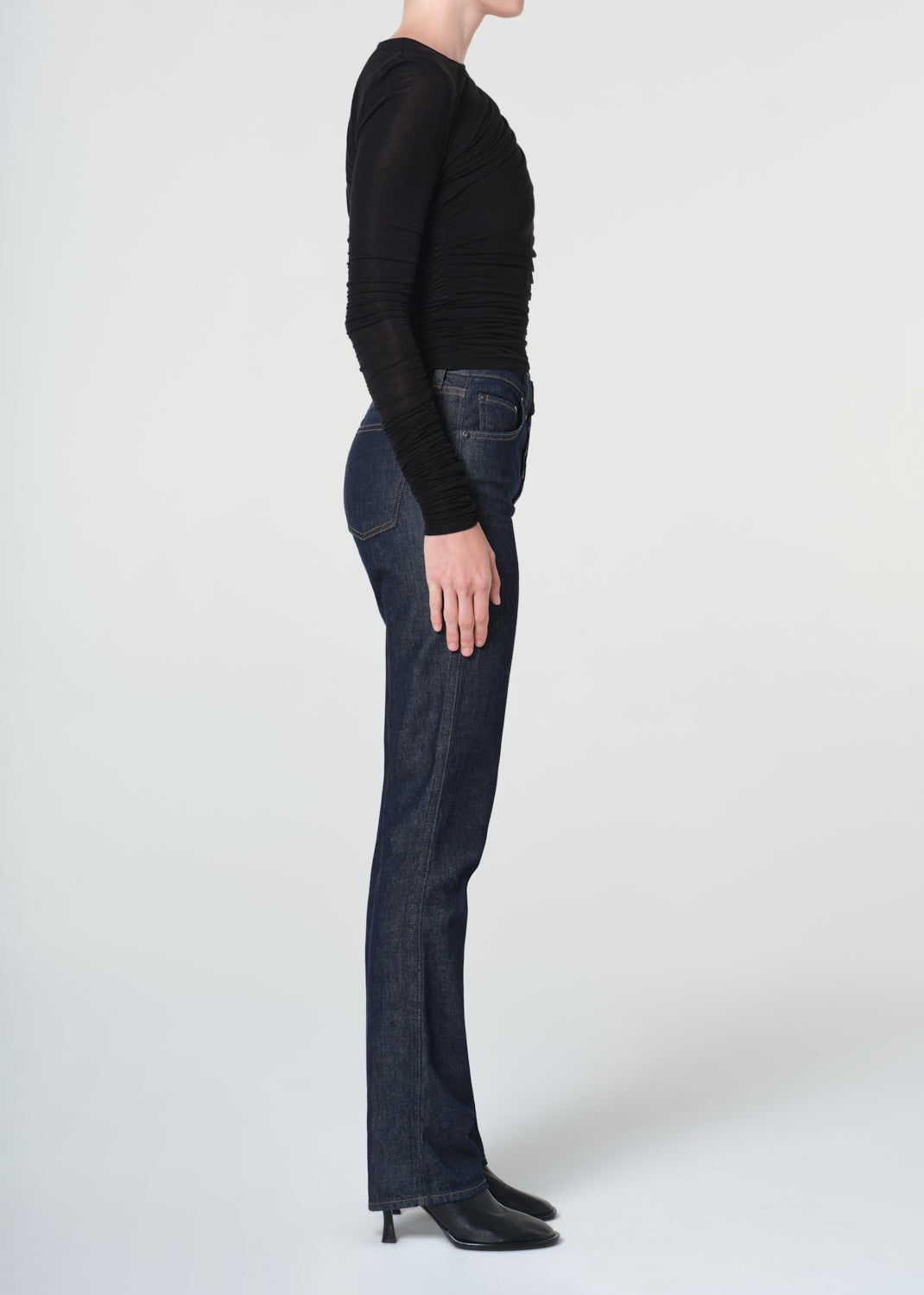 Person wearing a black sweater and dark jeans on a white background
