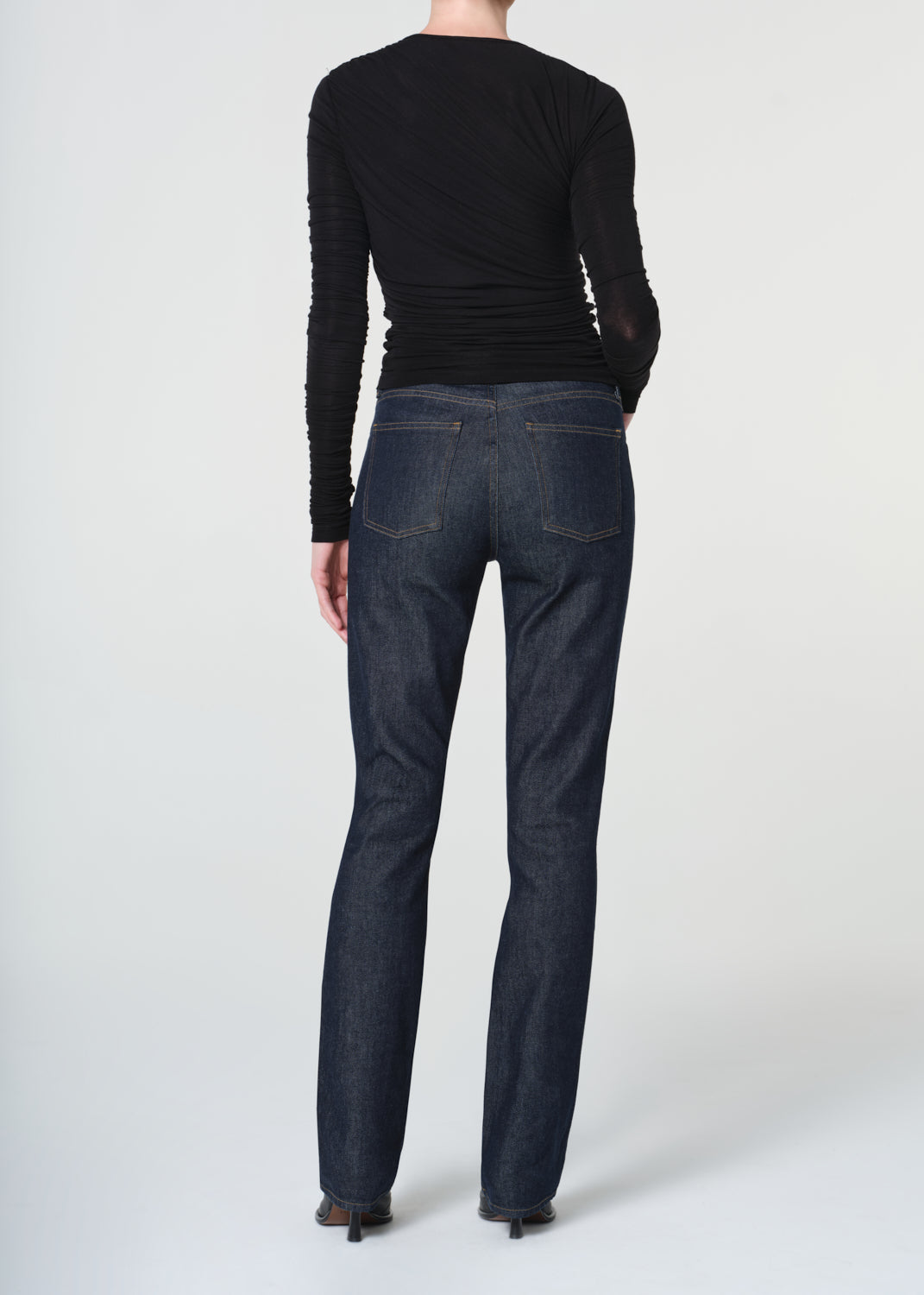 Person wearing a black long-sleeve top and dark blue jeans on a white background