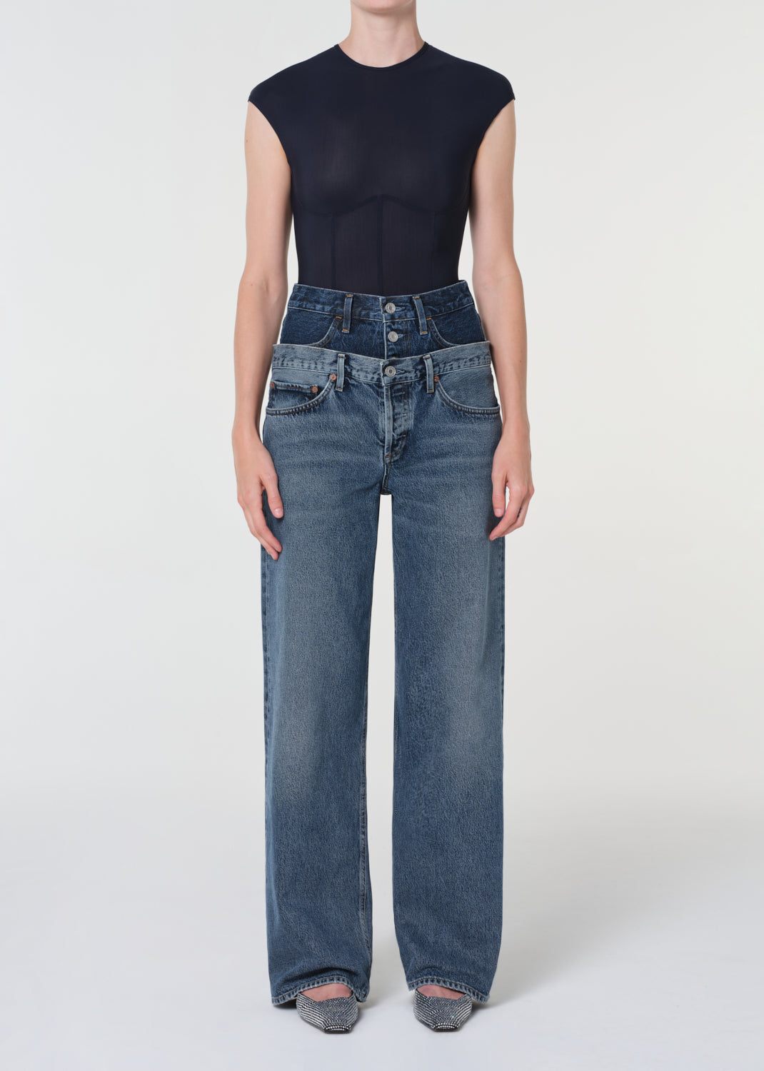 Person wearing high-waisted blue jeans and a black sleeveless top on a white background