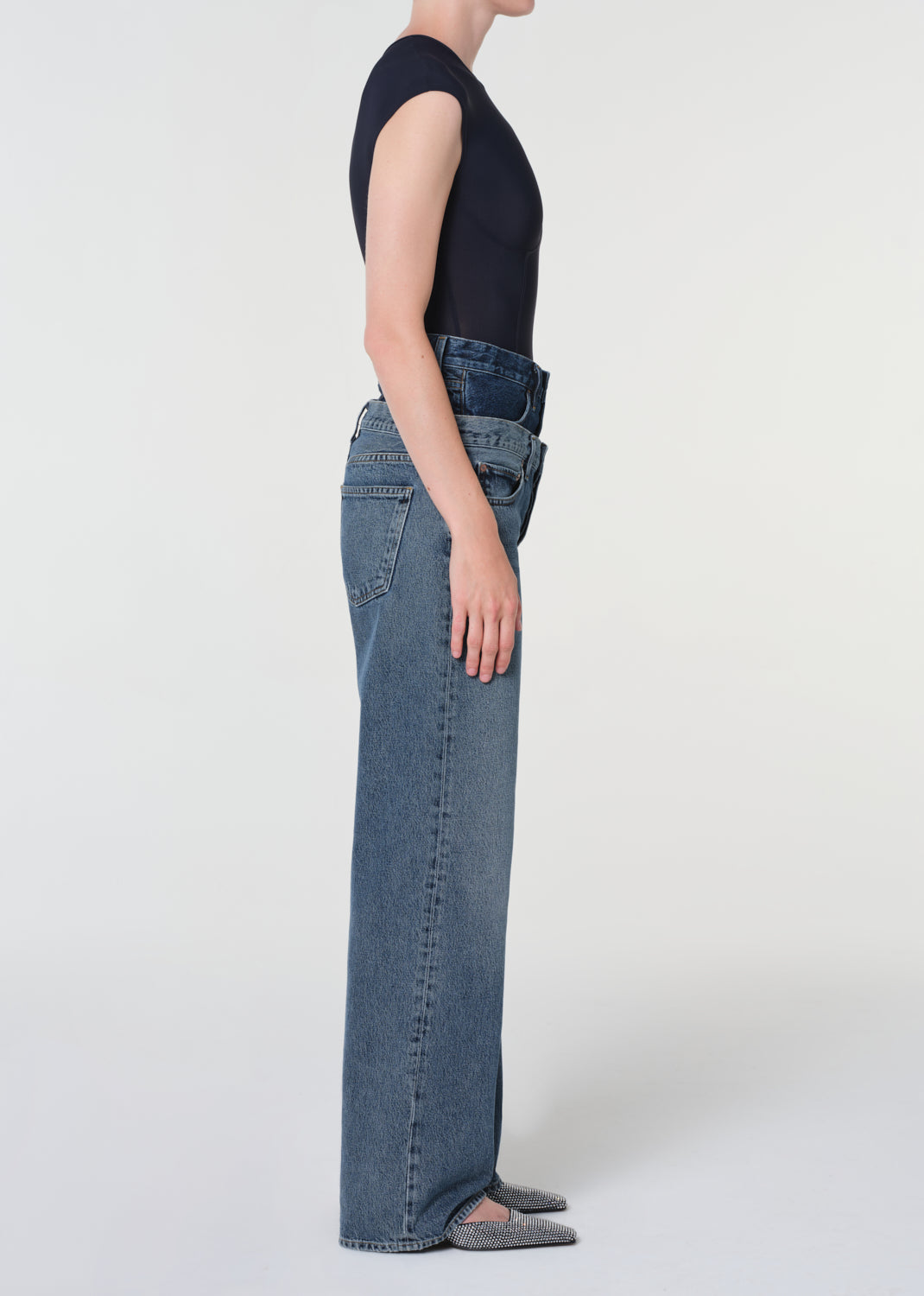 Person wearing blue jeans and a black top on a white background
