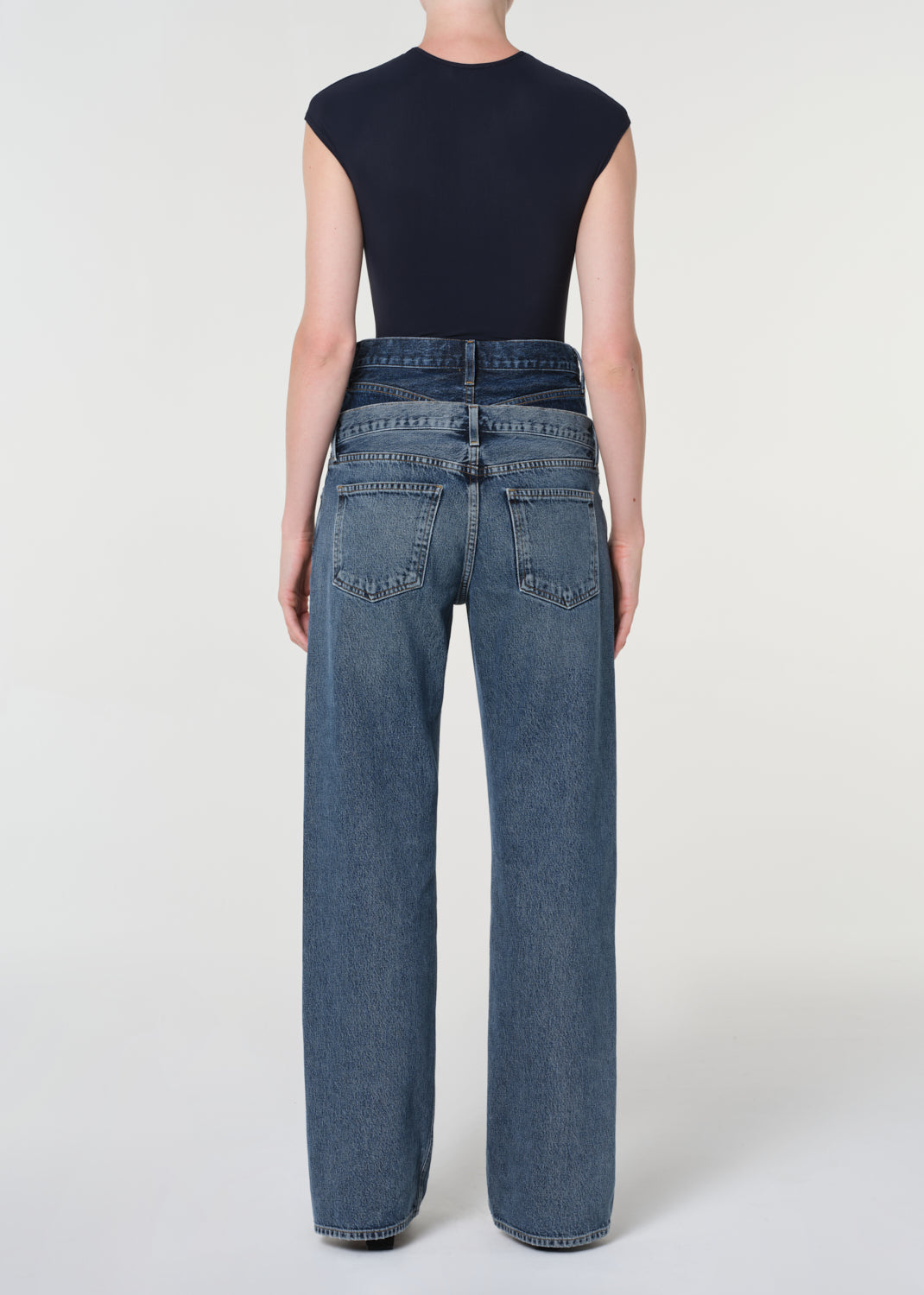 Person wearing blue jeans and a black top on a white background