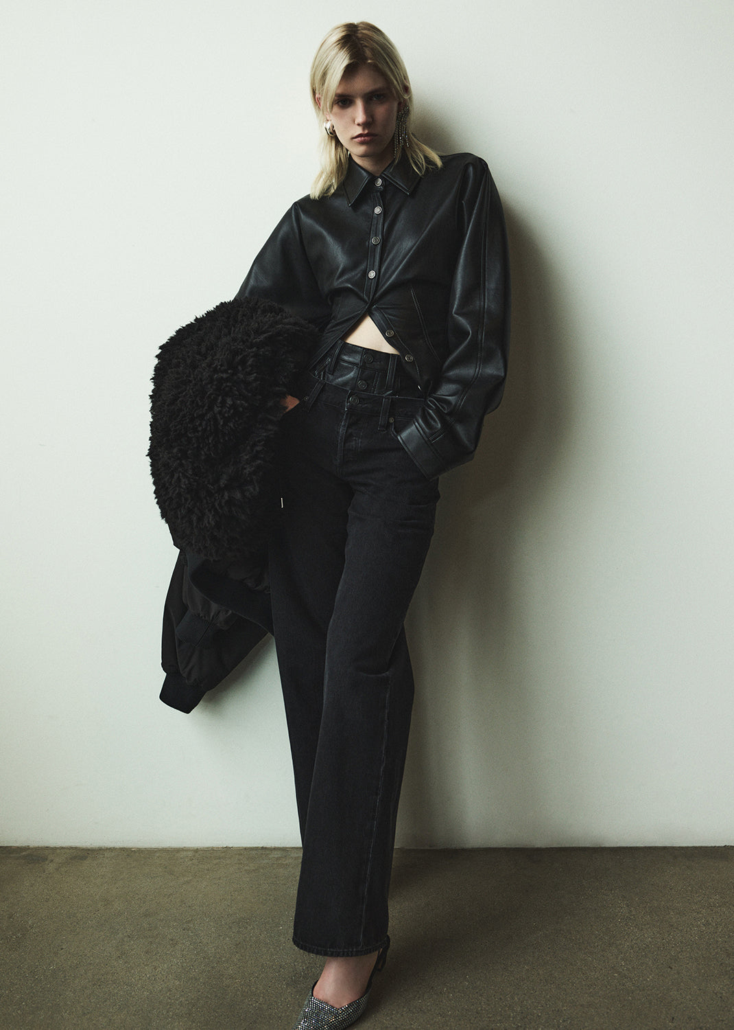 Person wearing a black leather outfit against a white wall