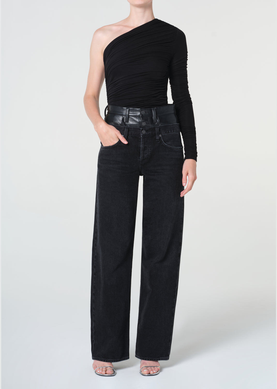 Person wearing a black one-shoulder top and black wide-leg jeans on a white background