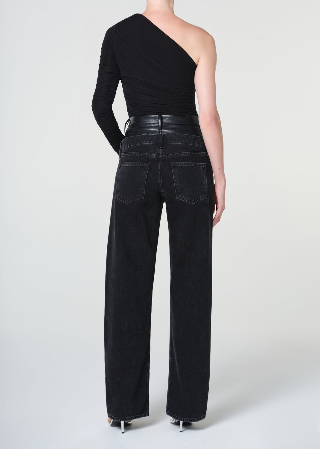 Person wearing a black one-shoulder top and black wide-leg pants on a white background