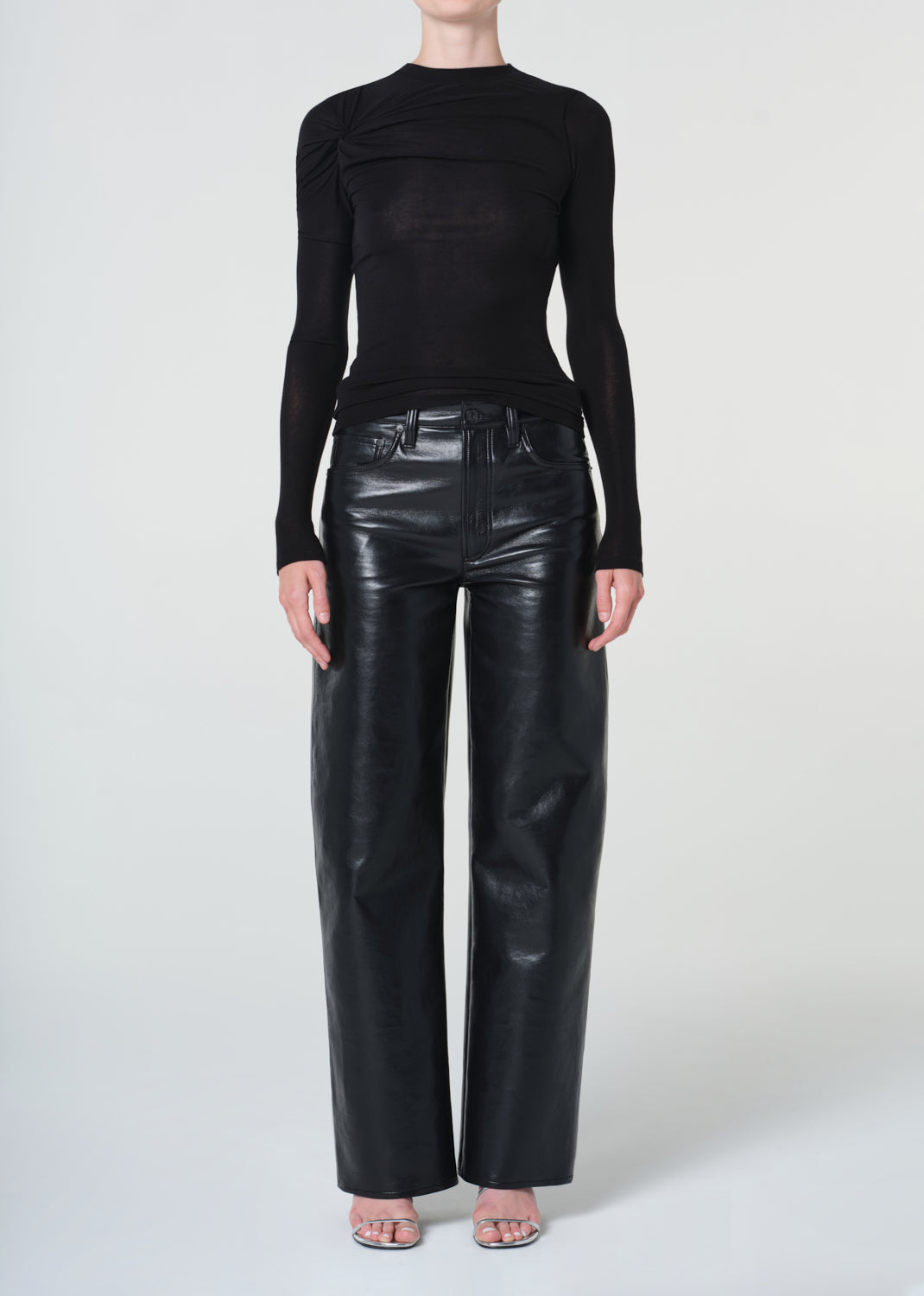 Person wearing a black long-sleeve top and black leather pants on a white background