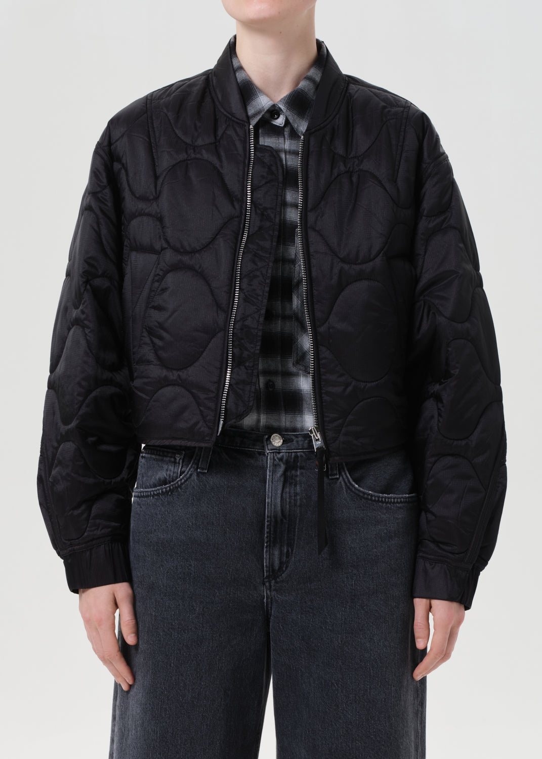 Person wearing a black quilted jacket over a patterned shirt on a white background