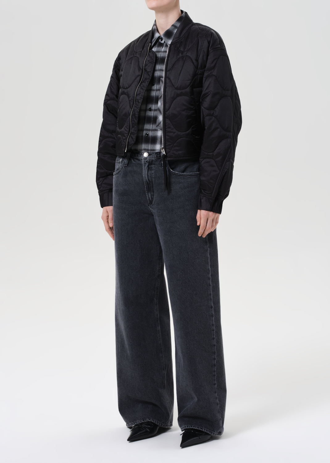Person wearing a black jacket, plaid shirt, and dark jeans on a white background