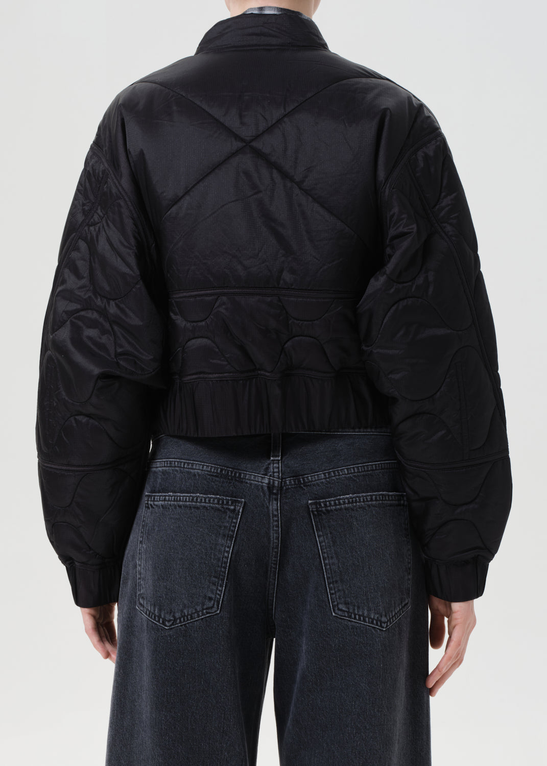 Person wearing a black jacket and dark jeans on a white background