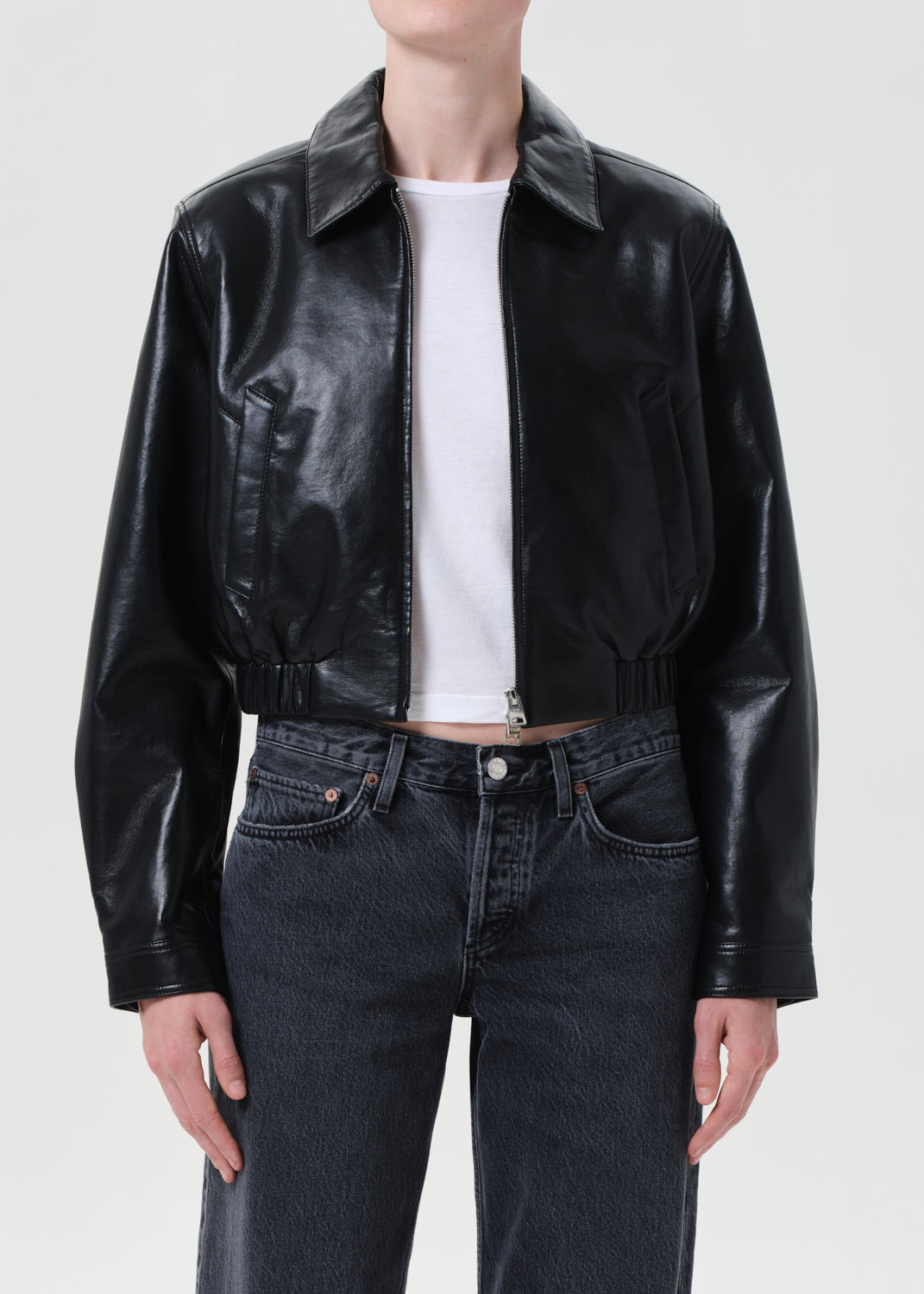 Person wearing a black leather jacket over a white shirt and dark jeans on a white background