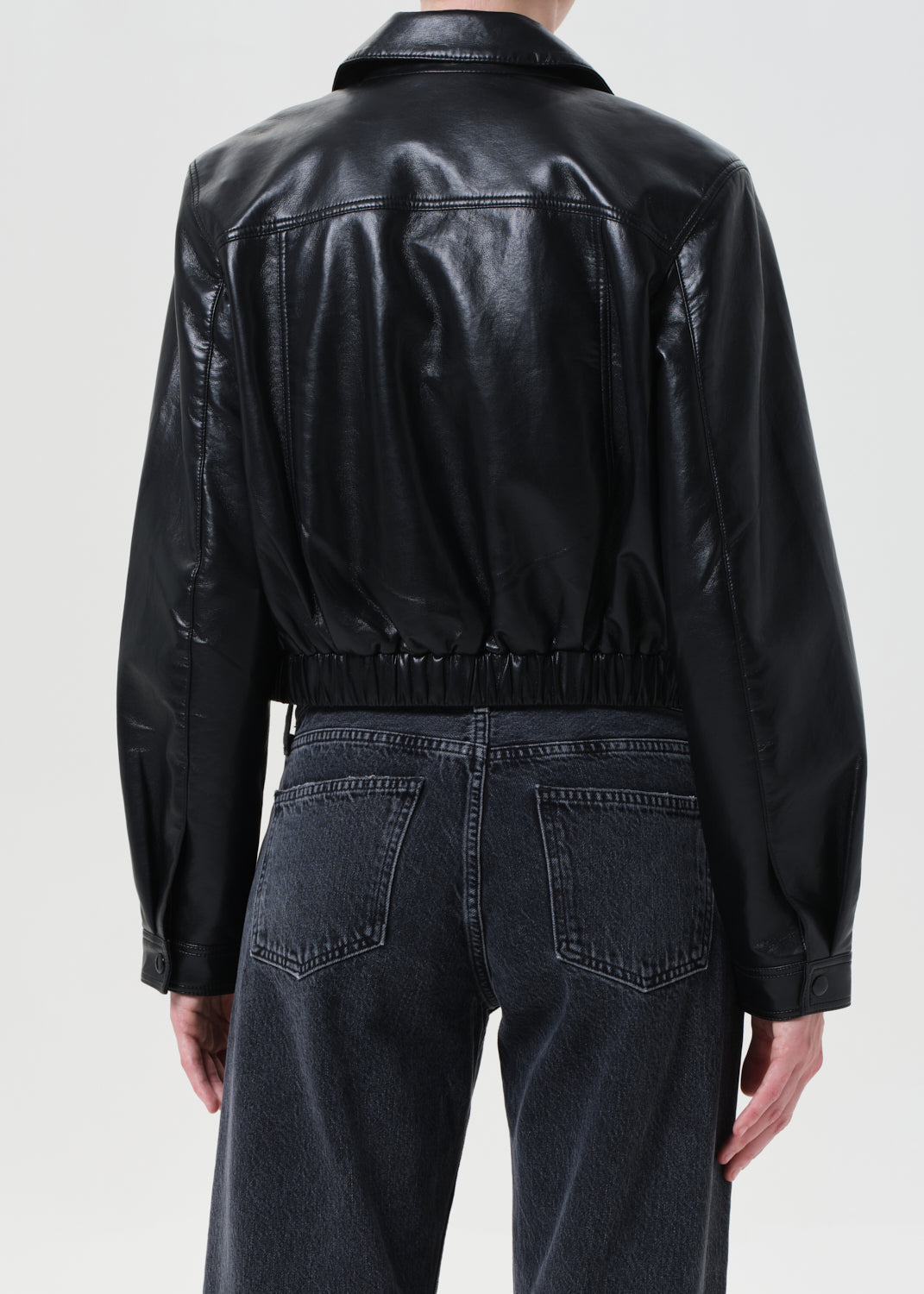 Person wearing a black leather jacket and dark jeans on a plain background