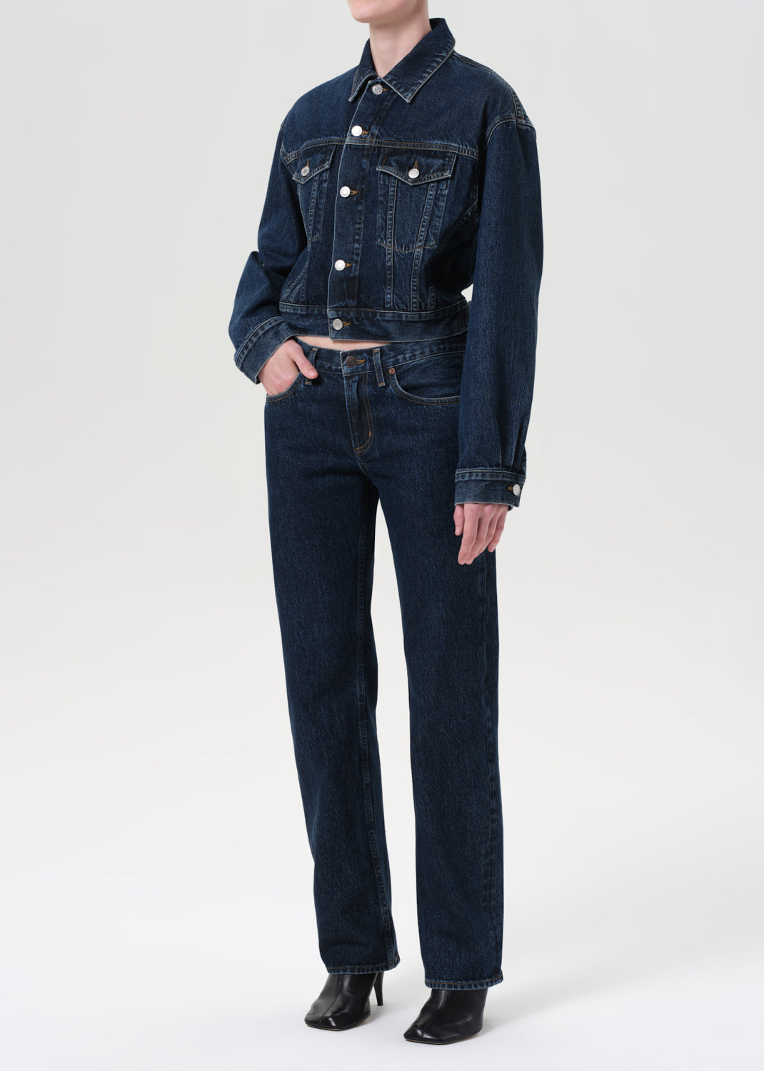 Person wearing a dark blue denim jacket and jeans on a white background