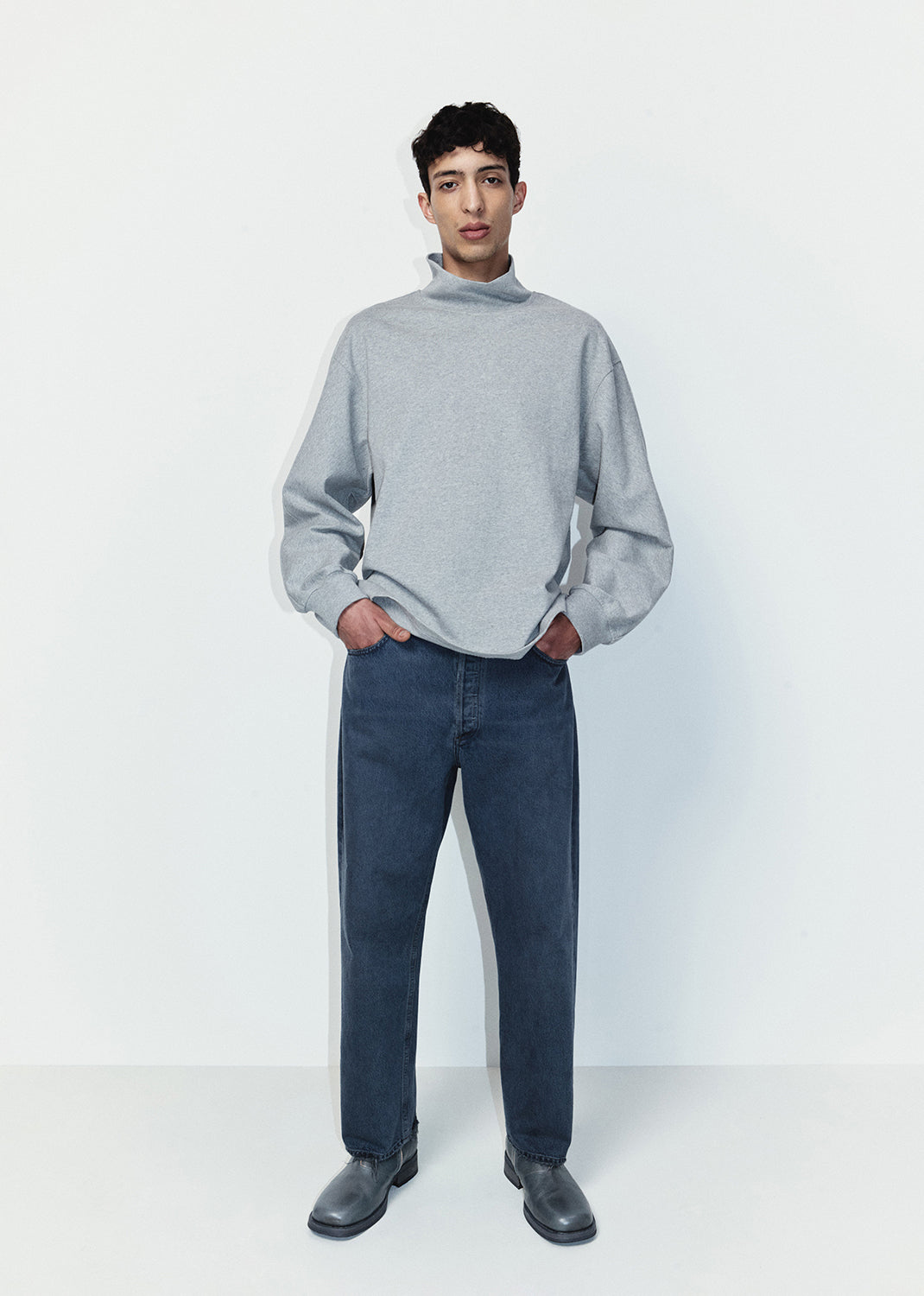 Man wearing a gray sweater and blue jeans standing against a white background