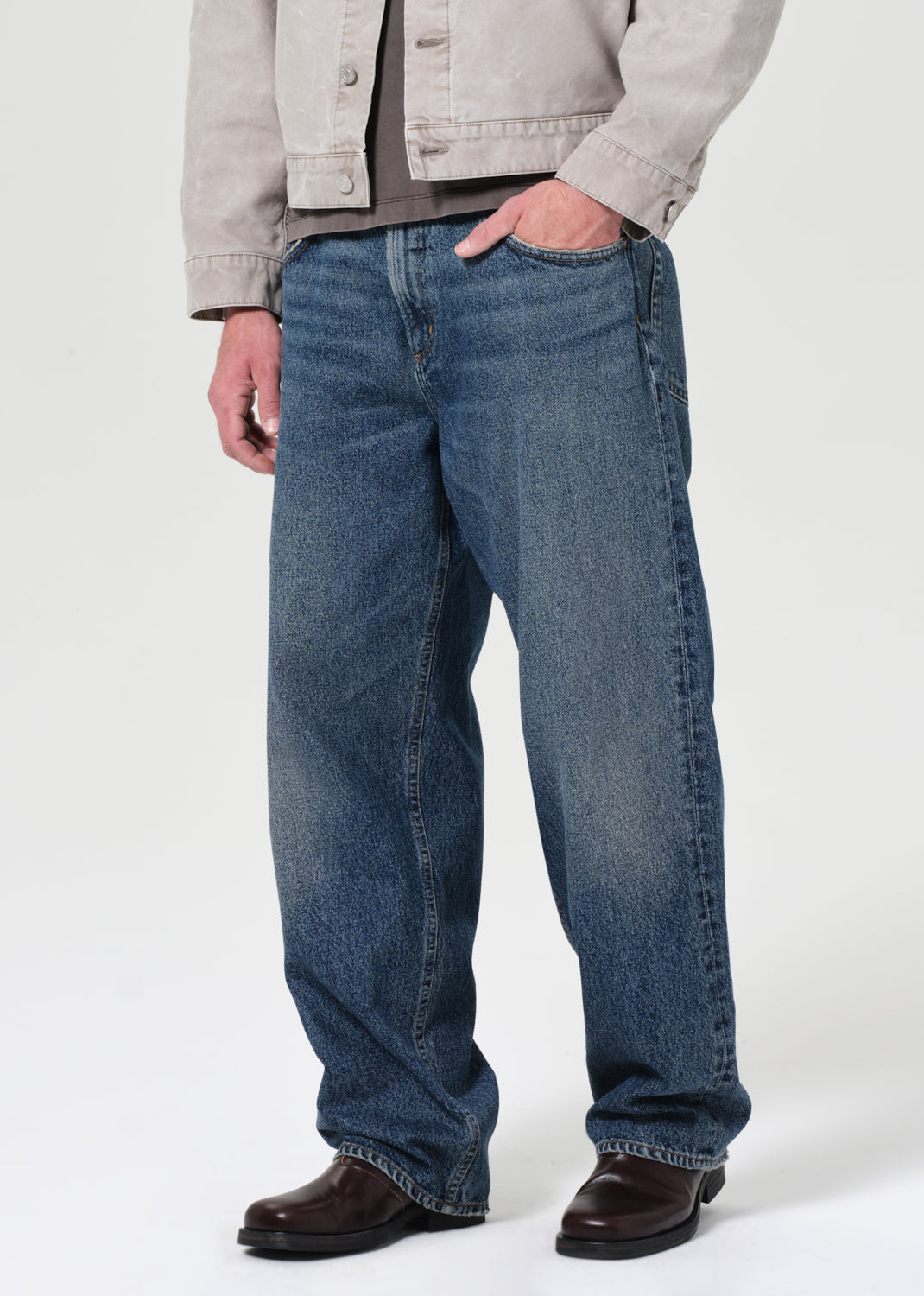 Person wearing blue jeans and a light gray jacket on a white background