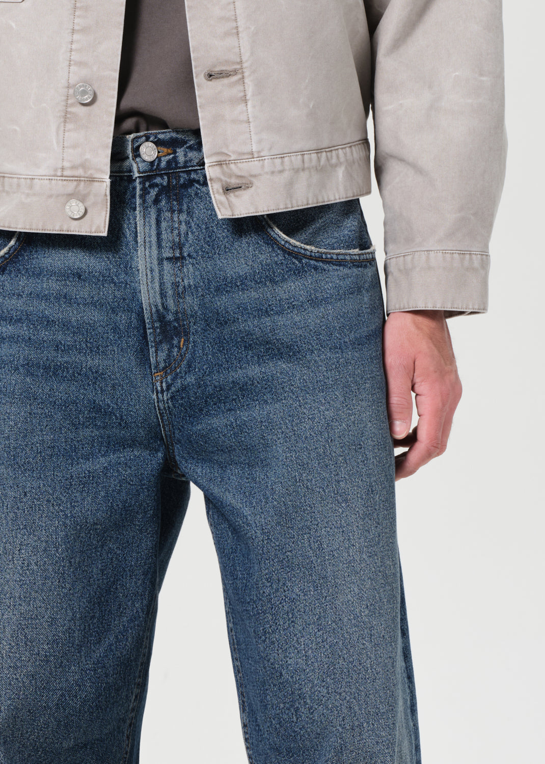 Person wearing blue jeans and a beige jacket on a plain background