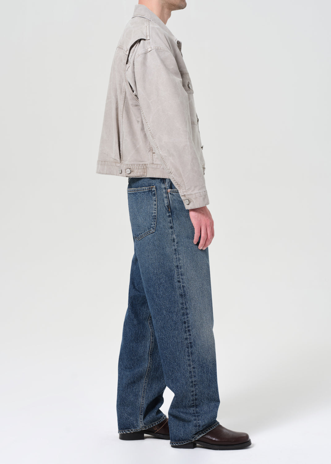 Person wearing a light gray jacket and blue jeans on a white background