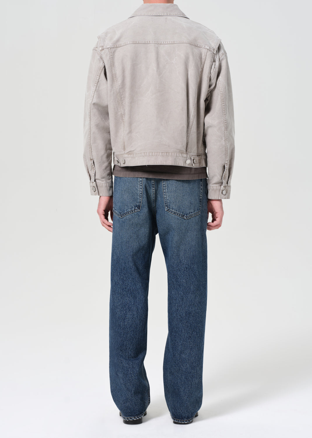 Person wearing a light gray jacket and blue jeans on a white background