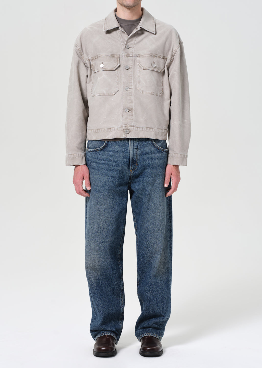Person wearing a light gray jacket and blue jeans on a white background