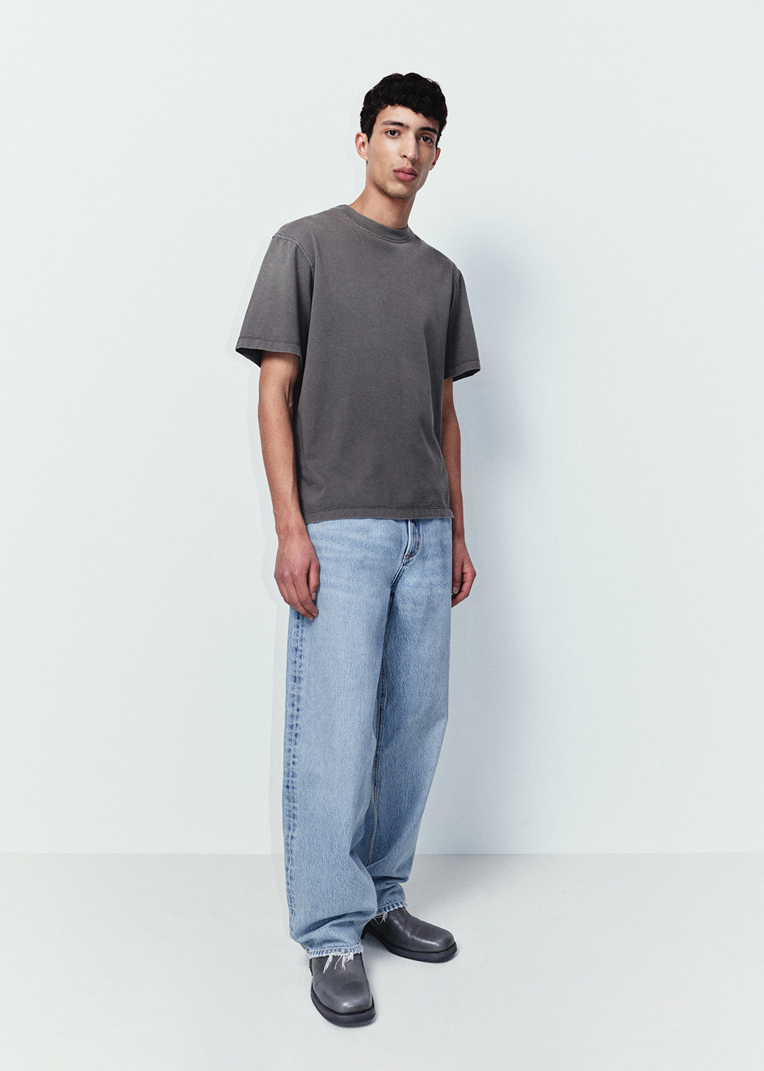 Person wearing a gray t-shirt and light blue jeans on a white background