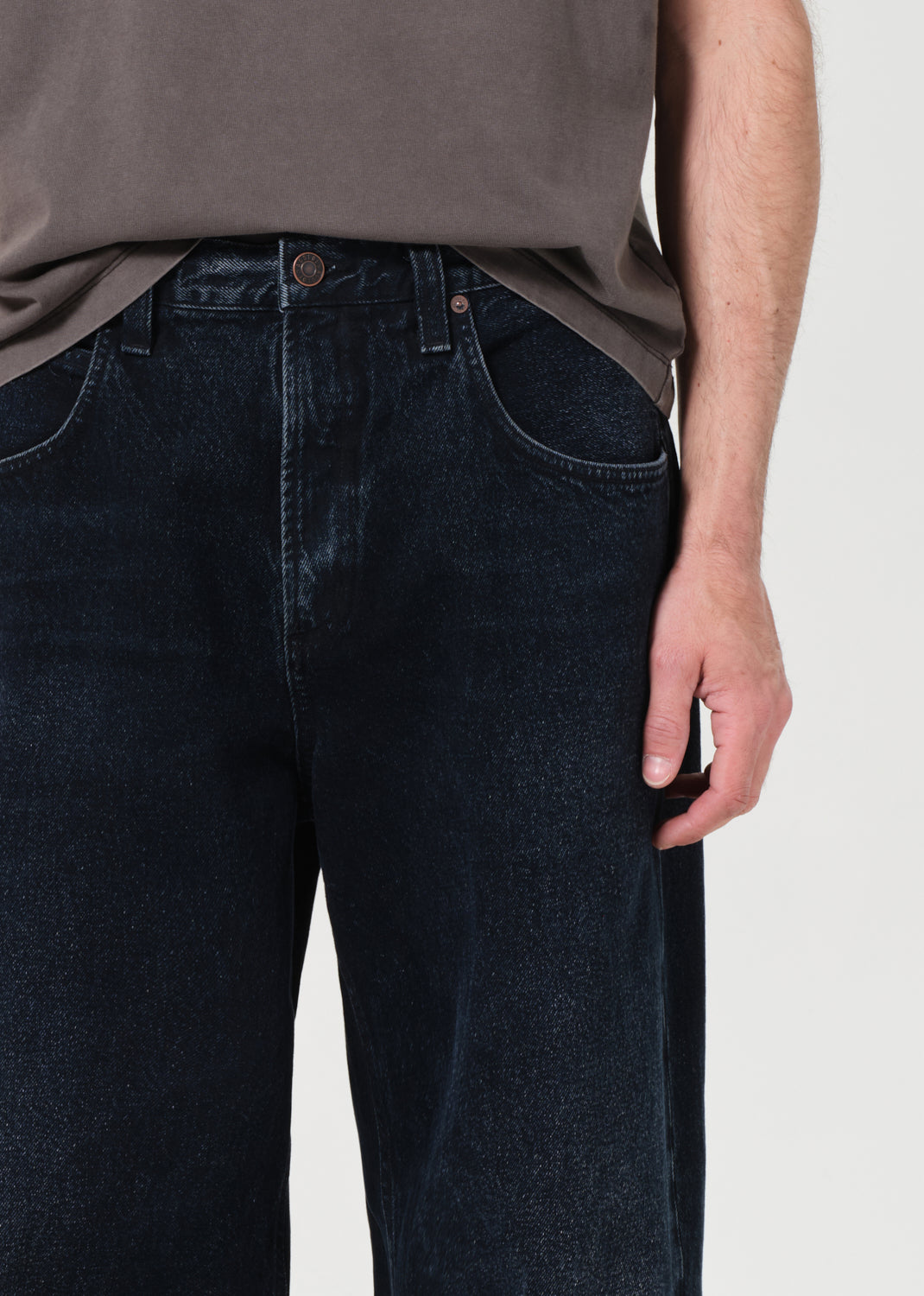 Person wearing dark blue jeans and a brown shirt on a light background