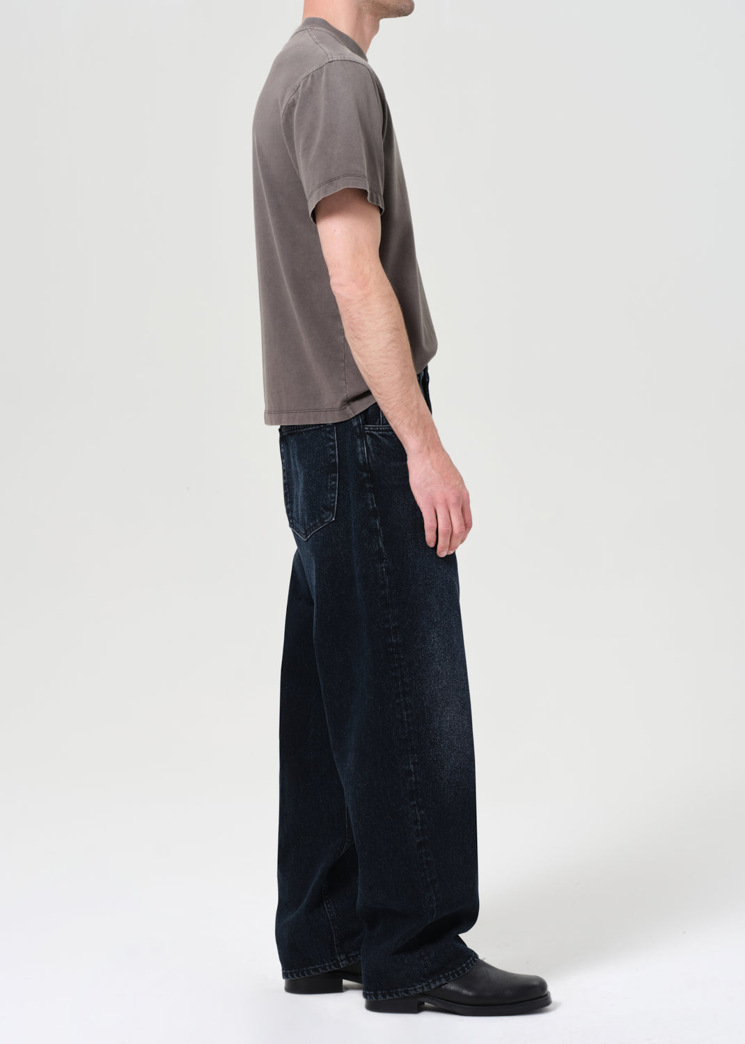 Person wearing a gray t-shirt and dark jeans on a white background