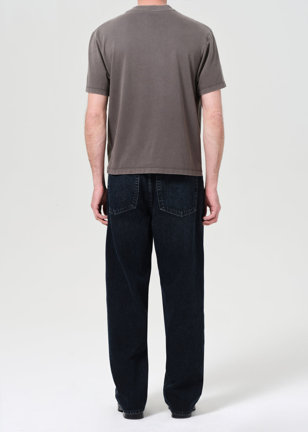 Person wearing a brown t-shirt and dark jeans on a white background