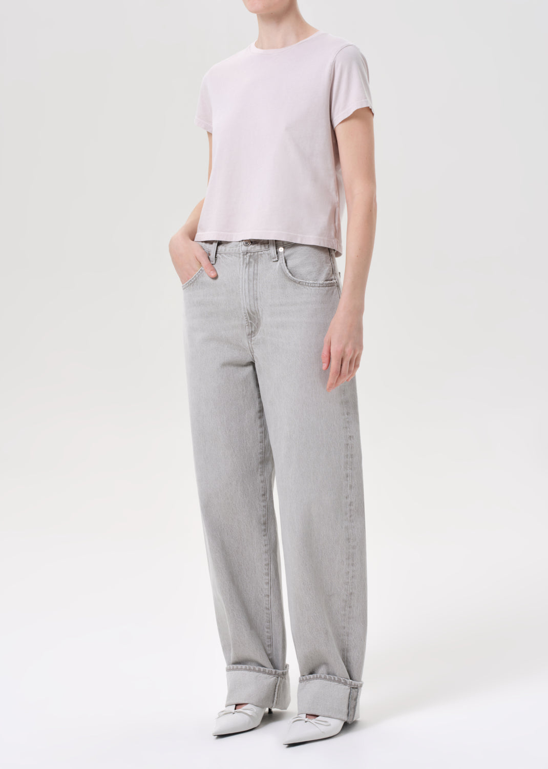 Person wearing a light pink t-shirt and gray jeans on a white background