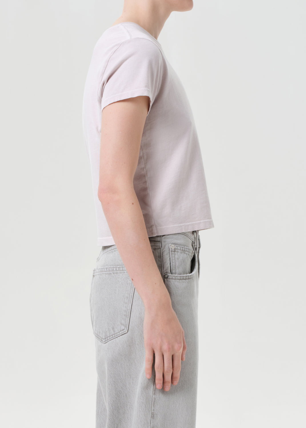 Person wearing a light purple t-shirt and light gray jeans on a plain background