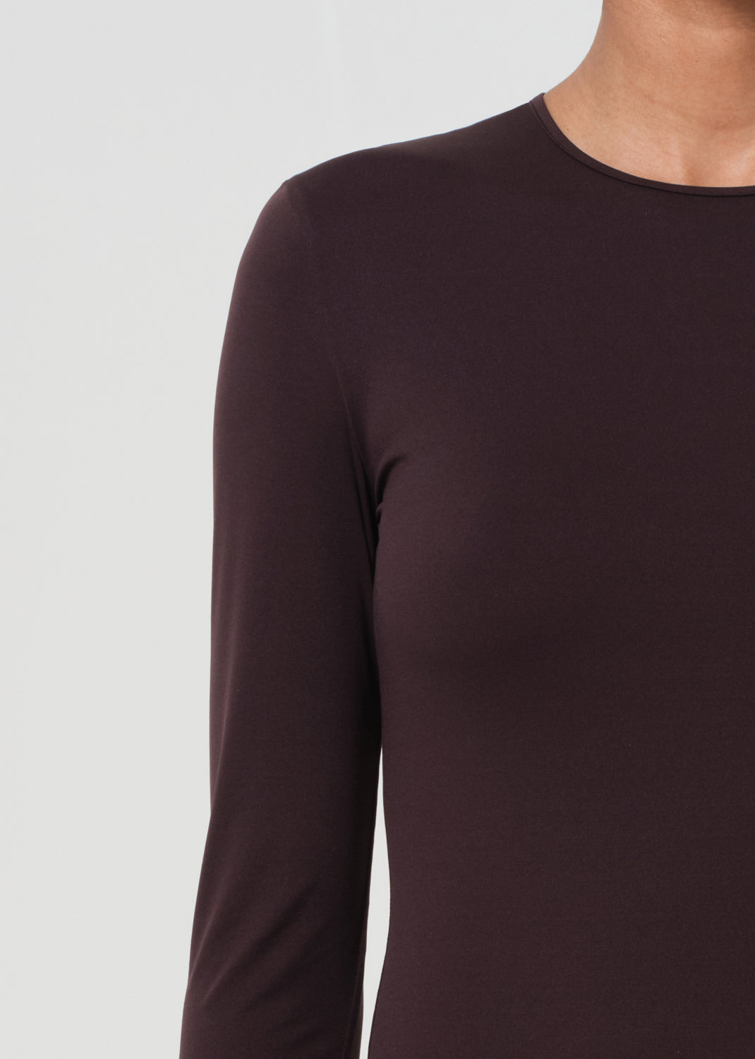 Close-up of a person wearing a dark brown long-sleeve top against a light gray background