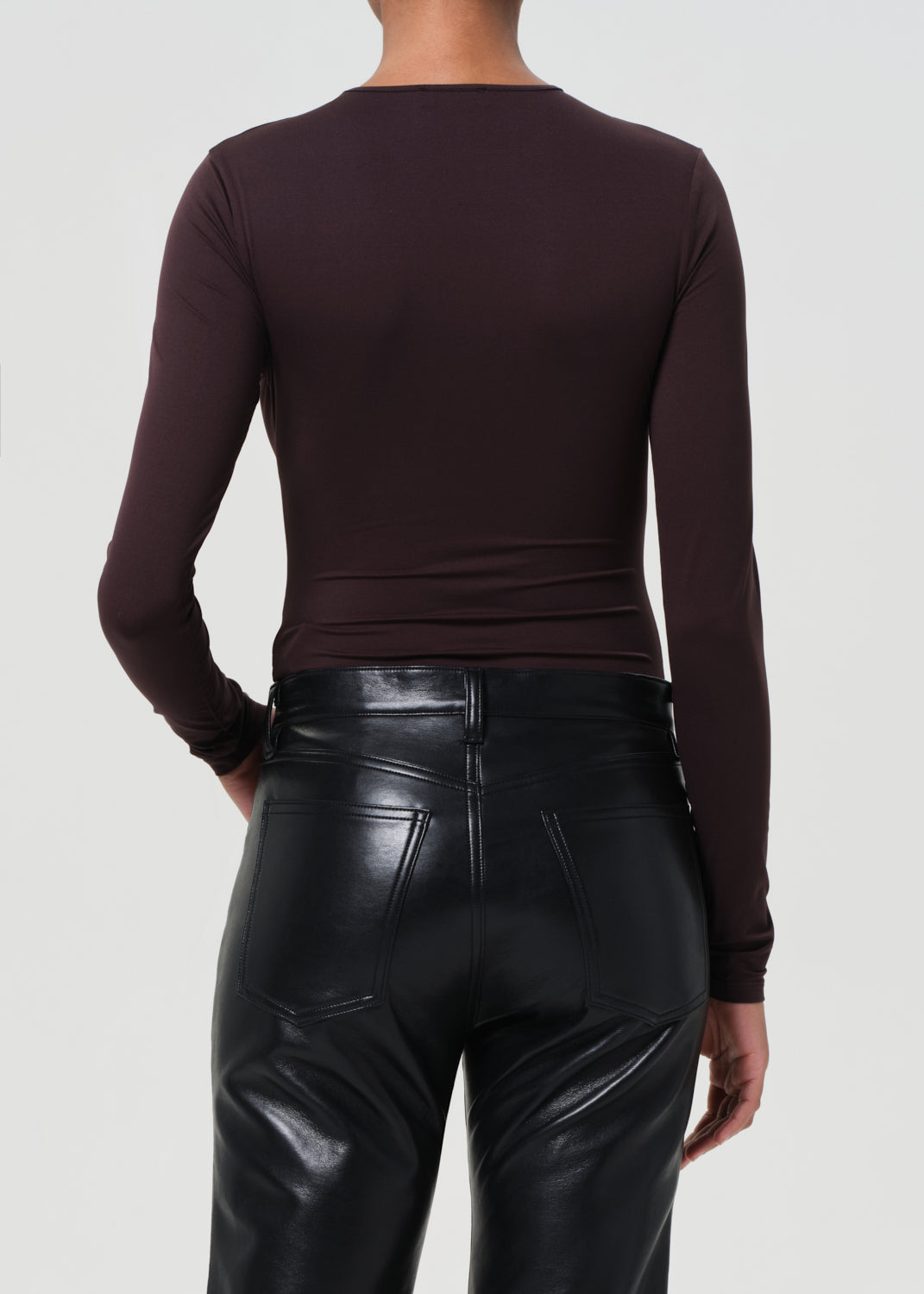 Person wearing a brown long-sleeve top and black leather pants on a white background