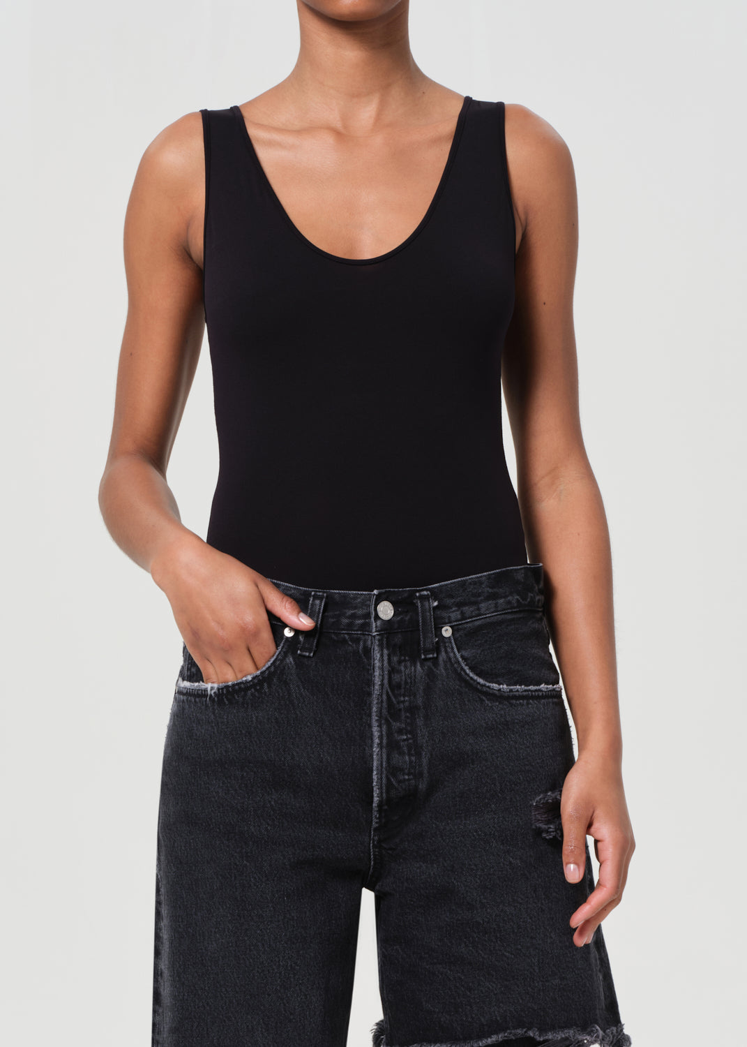 Person wearing a black tank top and black jeans on a plain background