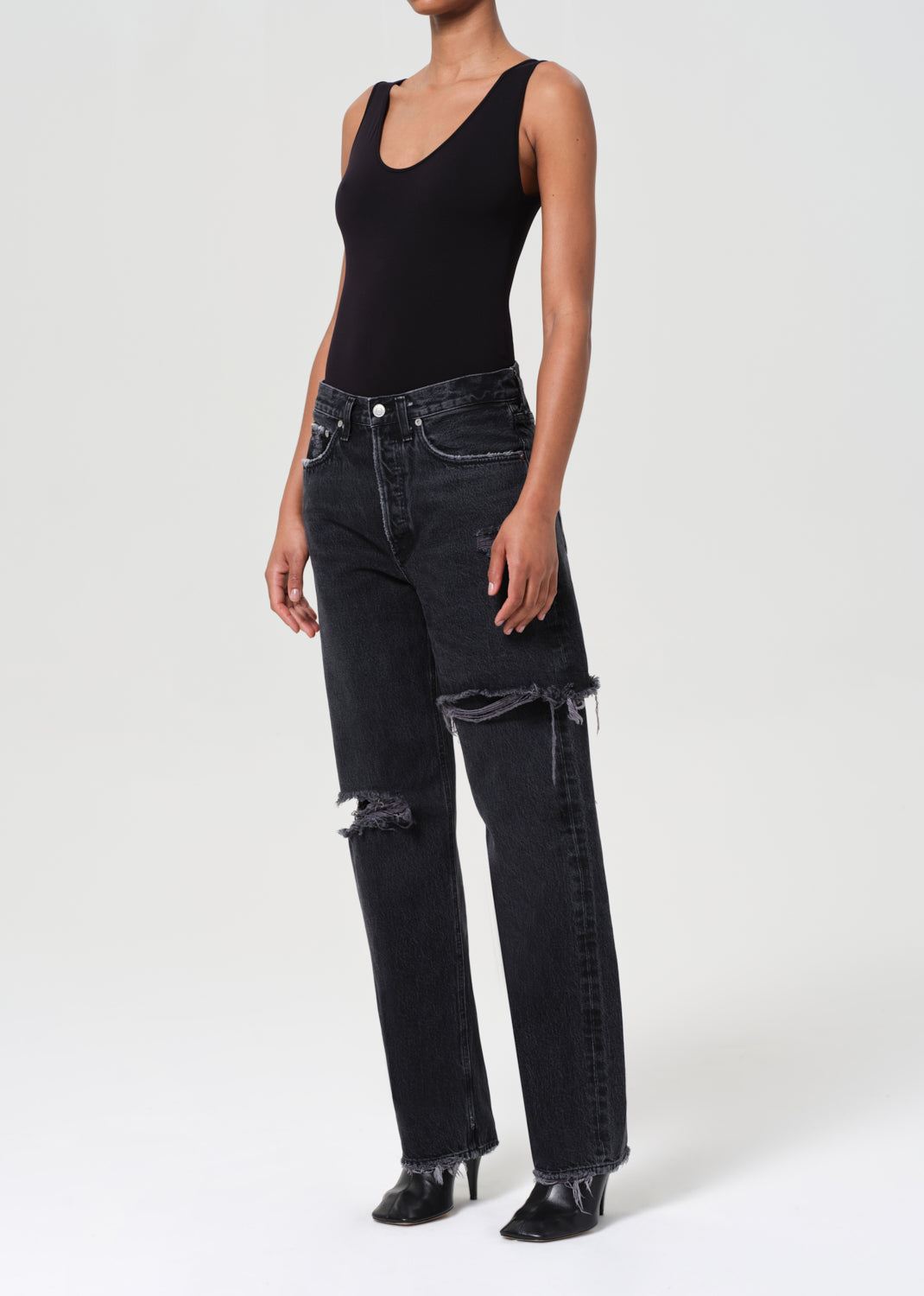 Person wearing black tank top and distressed black jeans on a white background