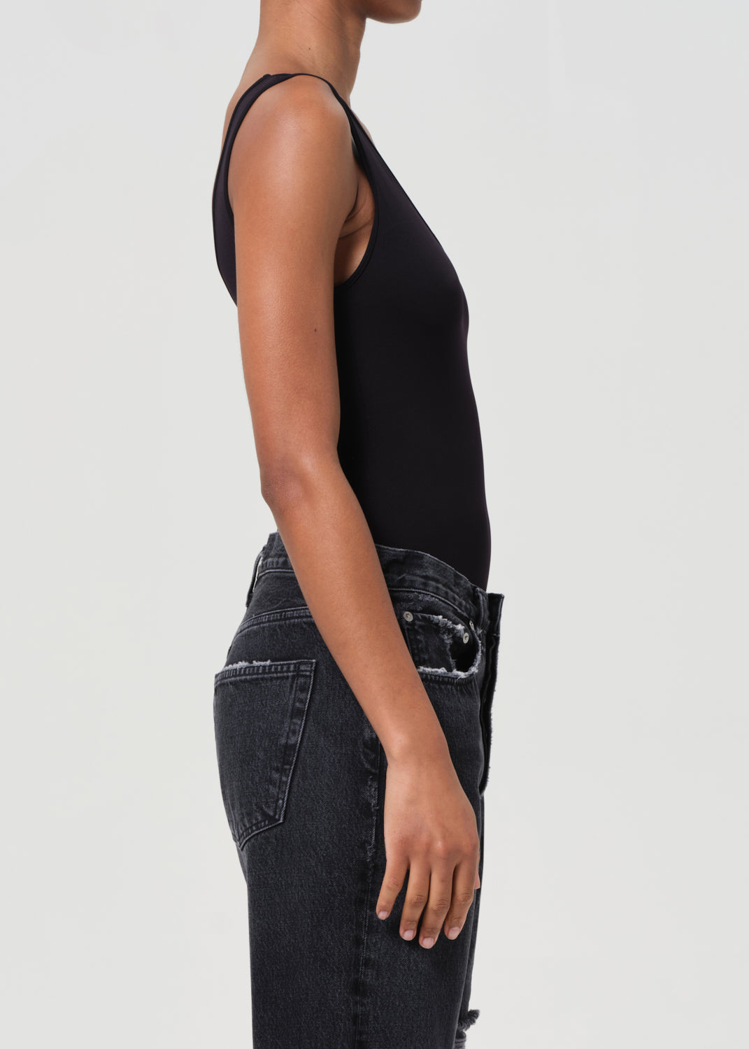 Person wearing a black tank top and black jeans on a light gray background