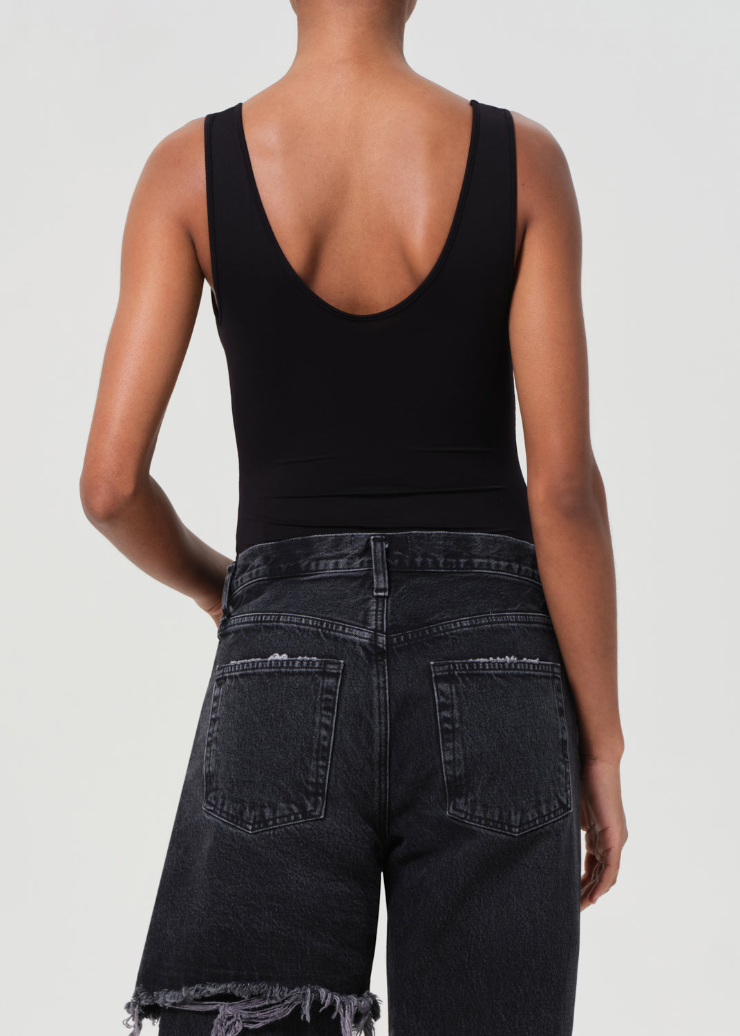 Person wearing a black tank top and dark jeans on a plain background