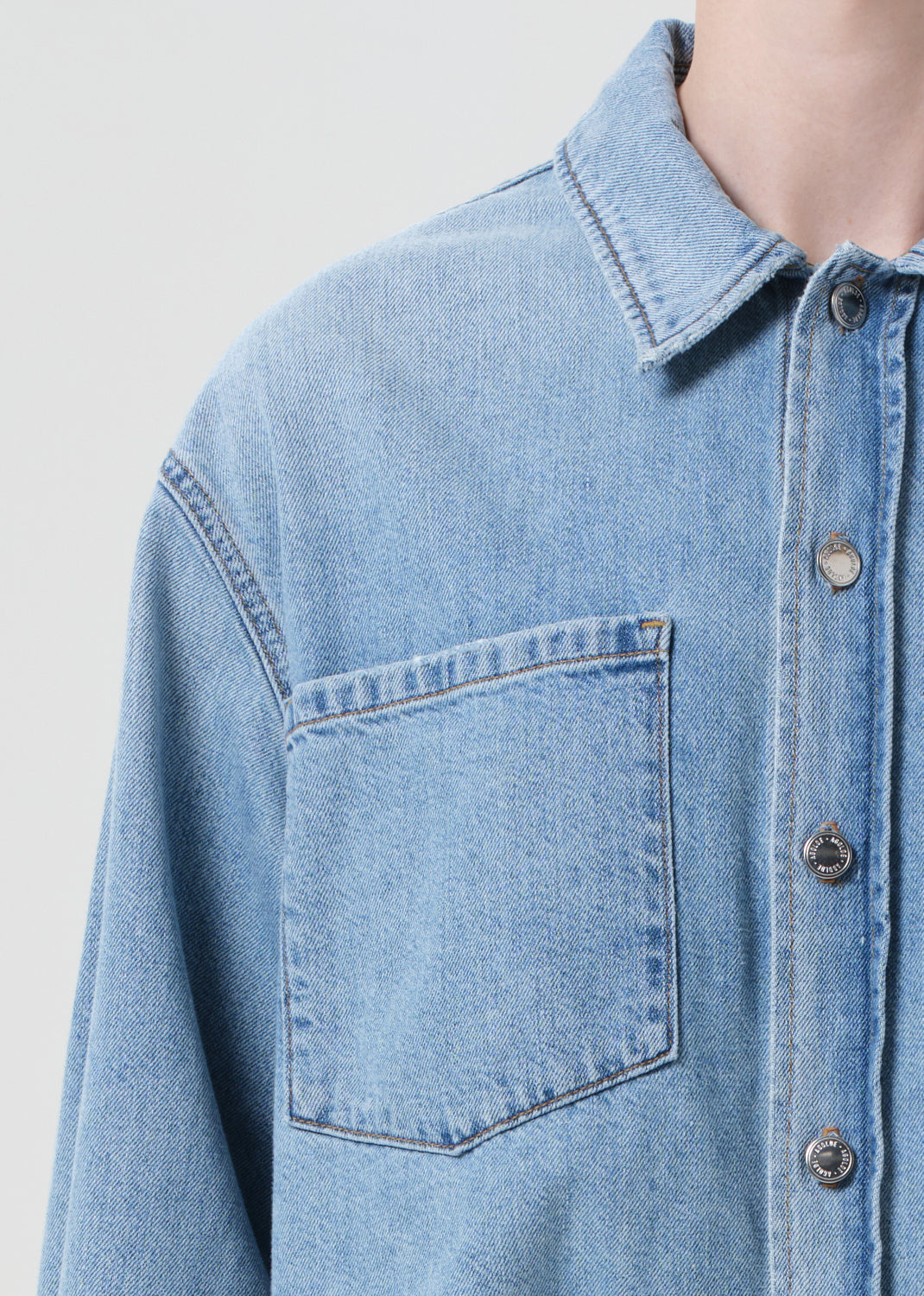 Close-up of a light blue denim shirt with a pocket on a plain background