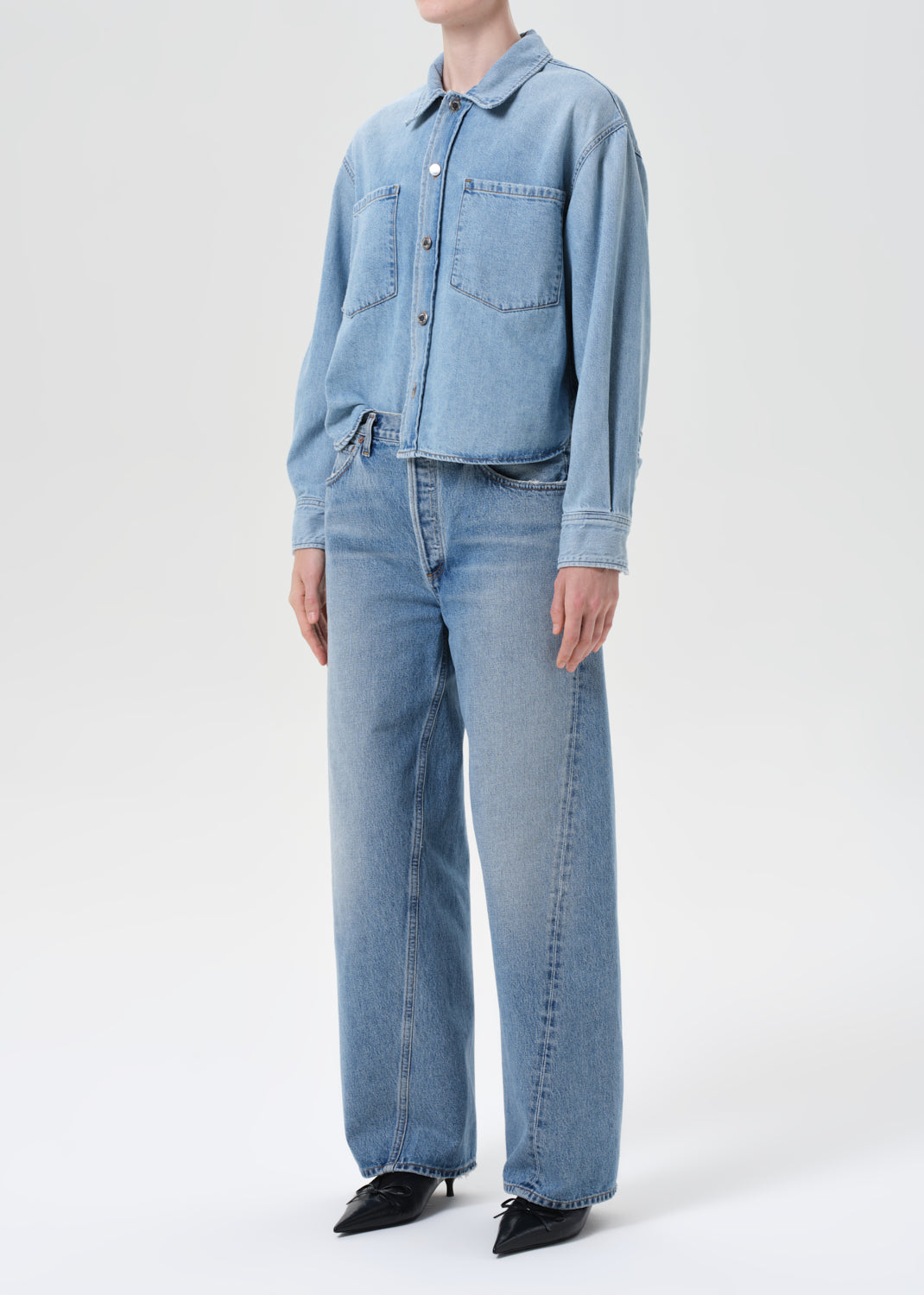 Person wearing a light blue denim jacket and jeans on a white background