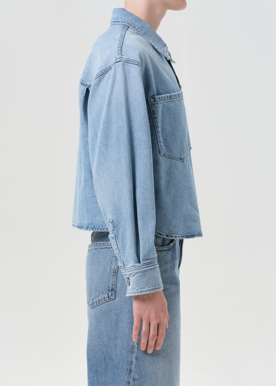 Person wearing a light blue denim jacket and jeans on a white background