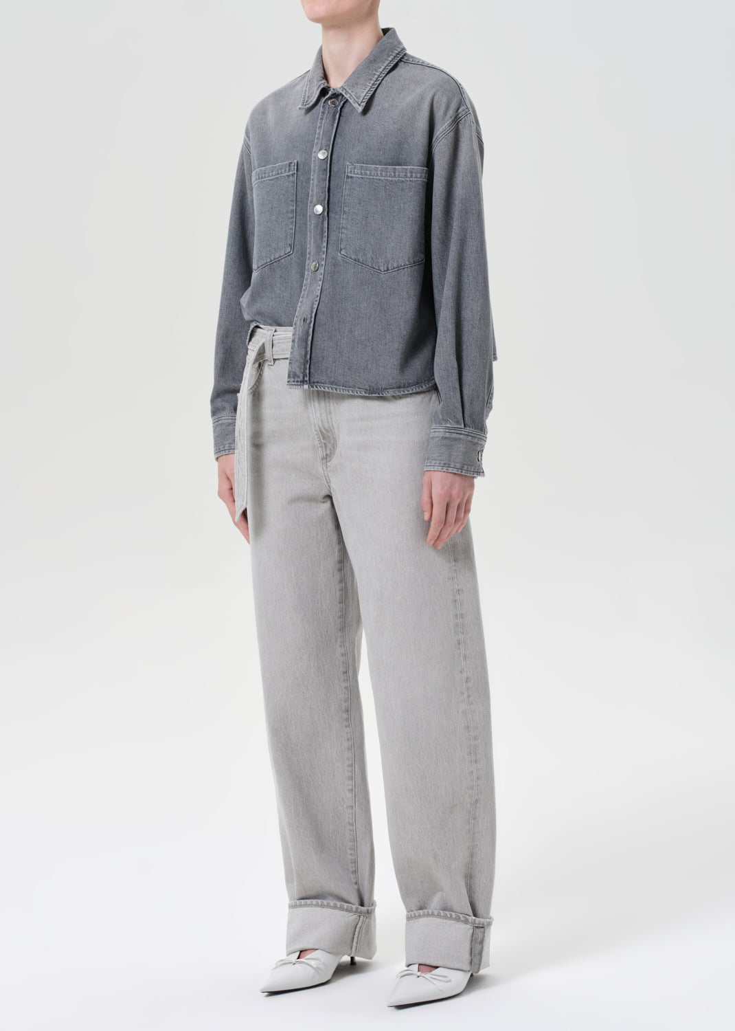 Person wearing a gray denim jacket and light gray pants on a white background