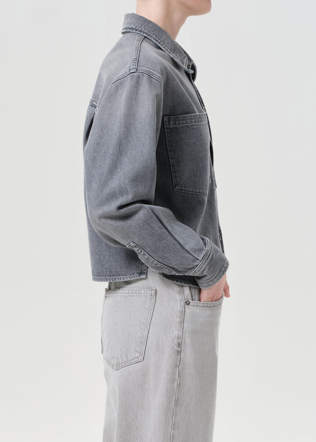 Person wearing a gray denim jacket and light gray pants on a white background