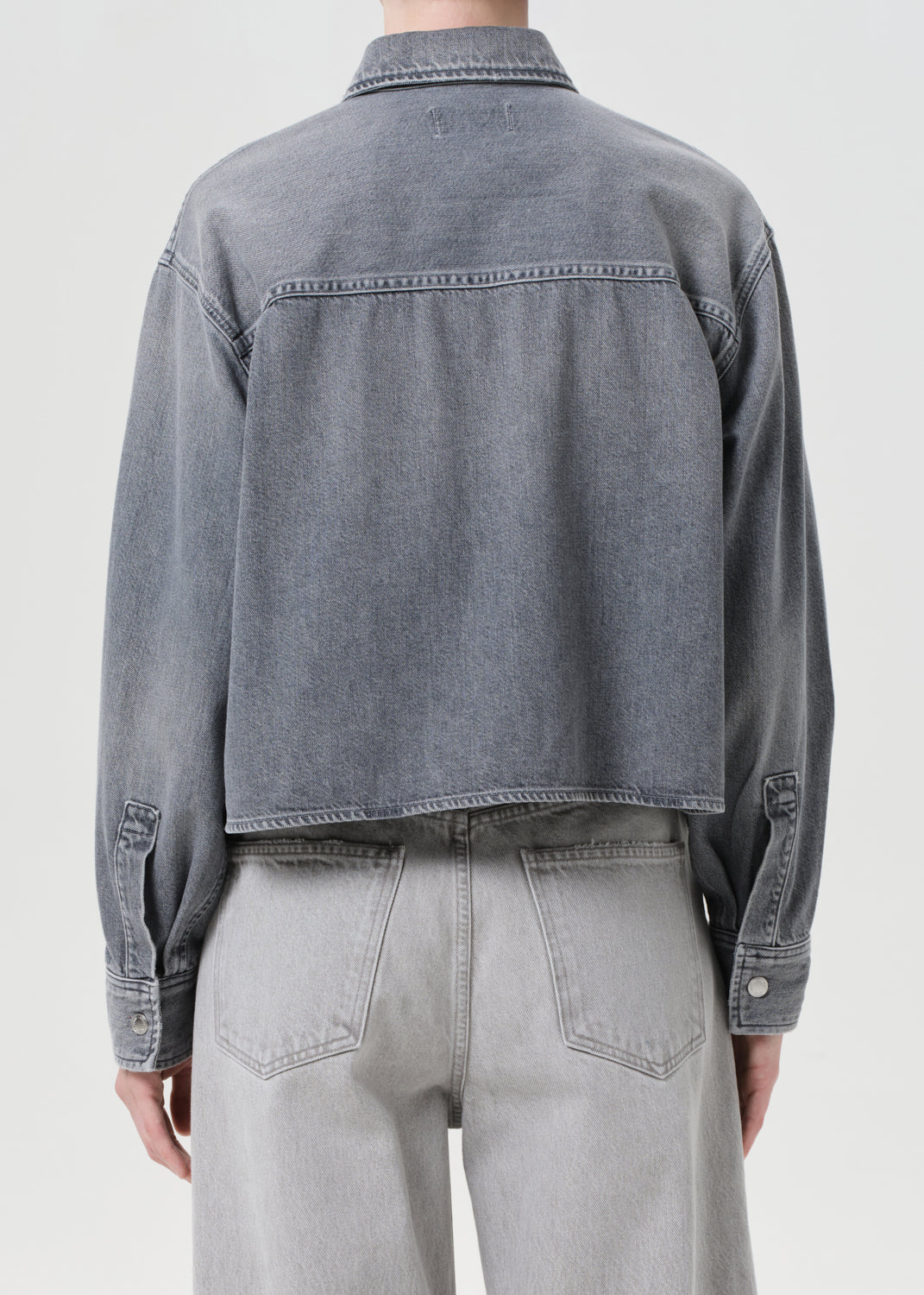Person wearing a gray denim jacket and pants on a white background