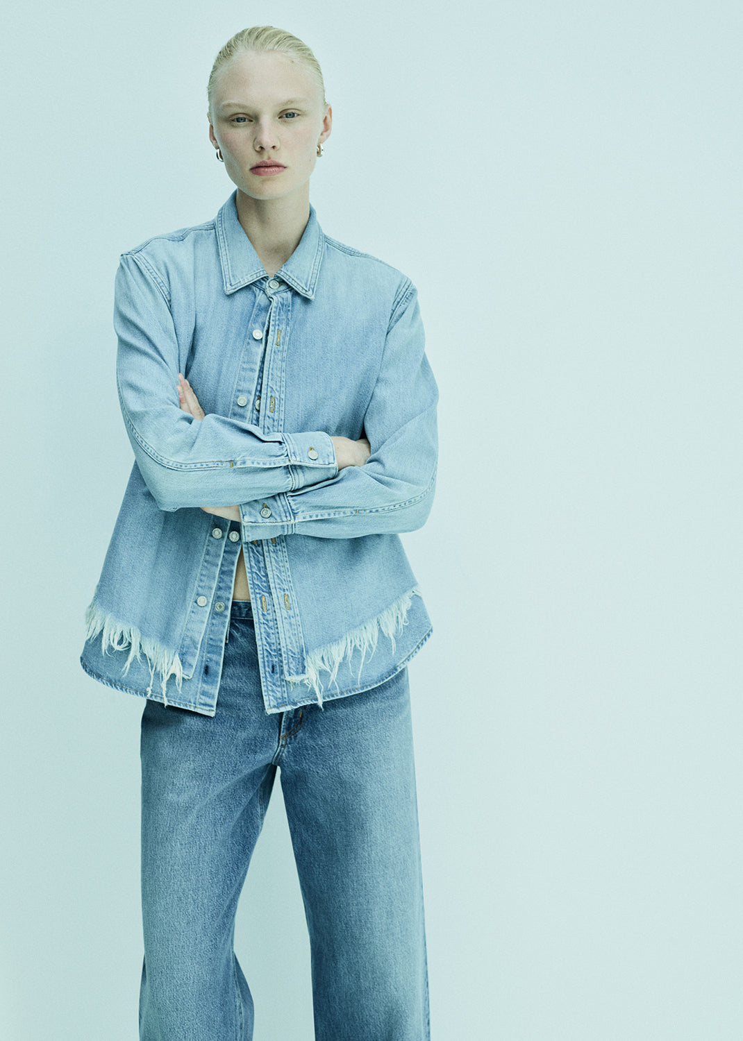 Person wearing a light blue denim jacket and jeans on a light blue background