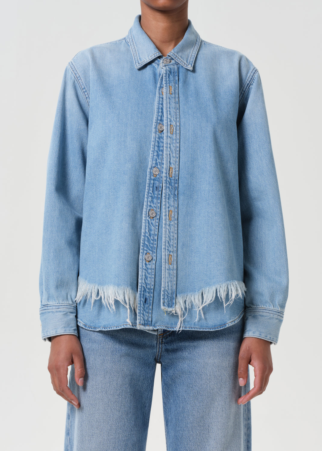 Person wearing a light blue denim jacket and jeans on a plain background