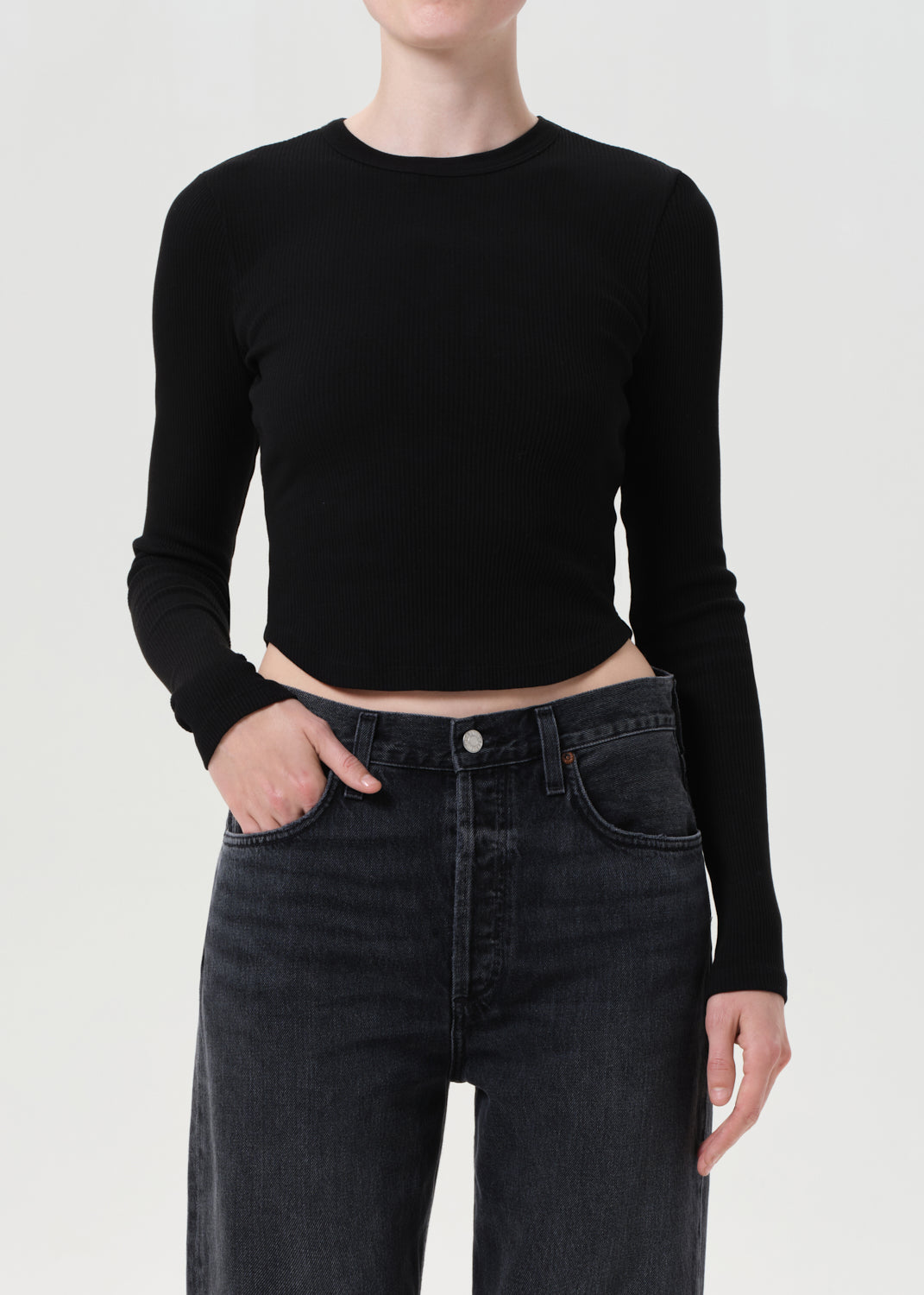 Person wearing a black long-sleeve crop top and dark jeans on a white background
