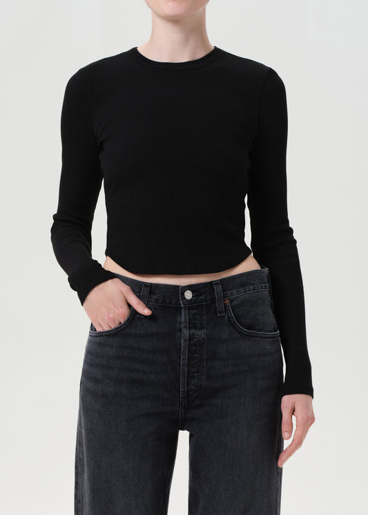 Person wearing a black long-sleeve crop top and dark jeans on a white background