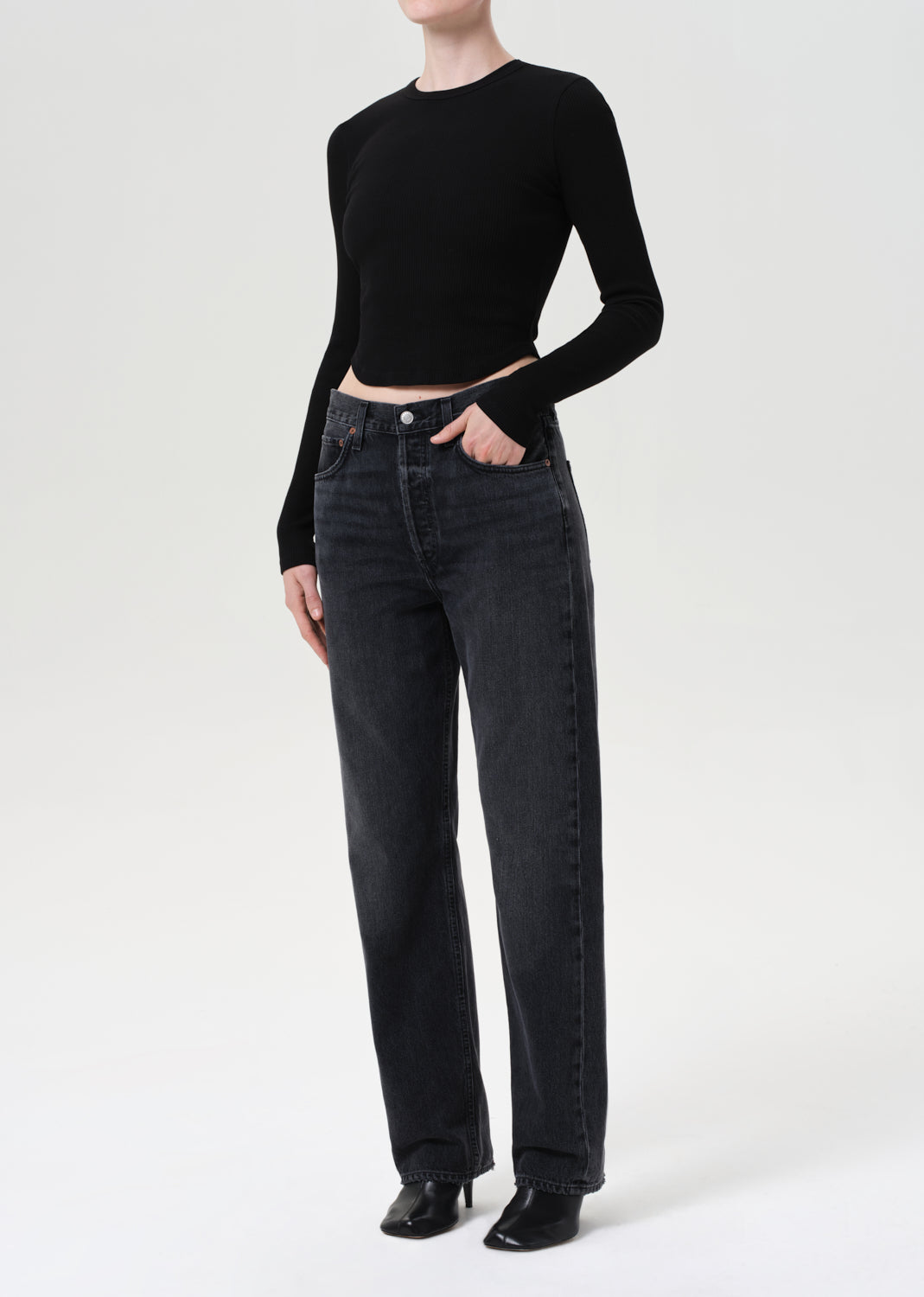 Person wearing a black long-sleeve top and dark jeans on a white background