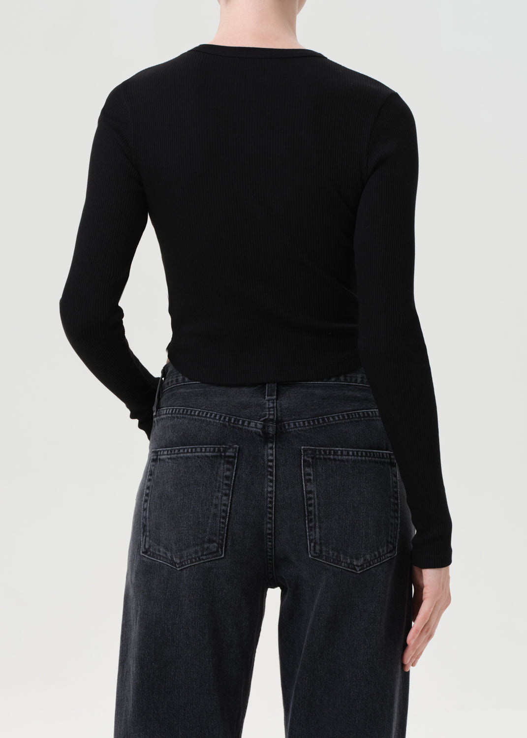 Person wearing a black long-sleeve top and dark jeans on a white background