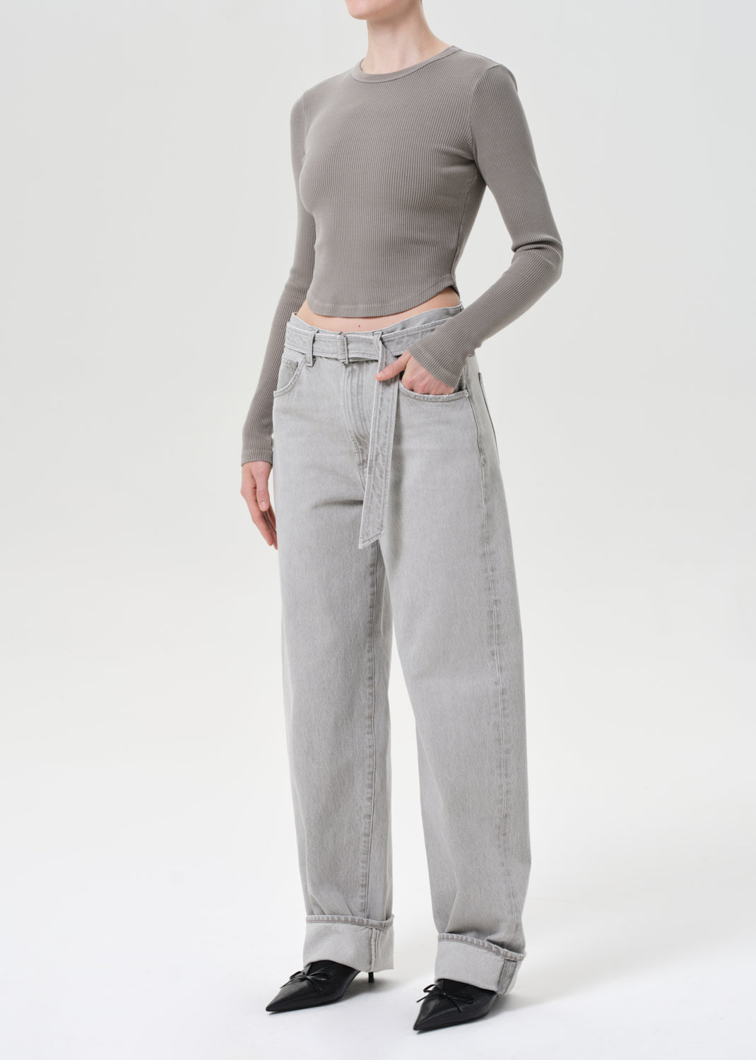 Person wearing a gray long-sleeve top and light gray jeans on a white background